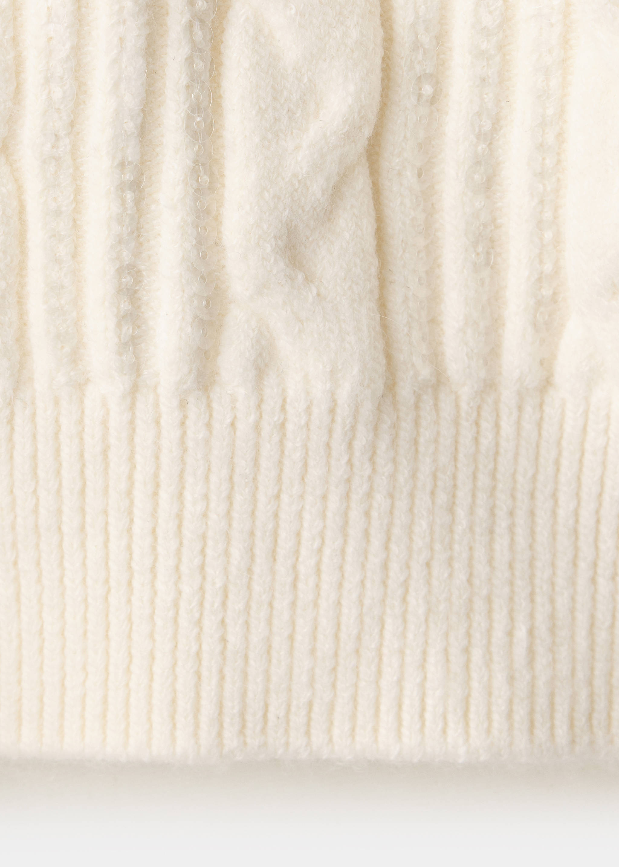 Close-up of a white cable-knit jumper texture with subtle sequins.