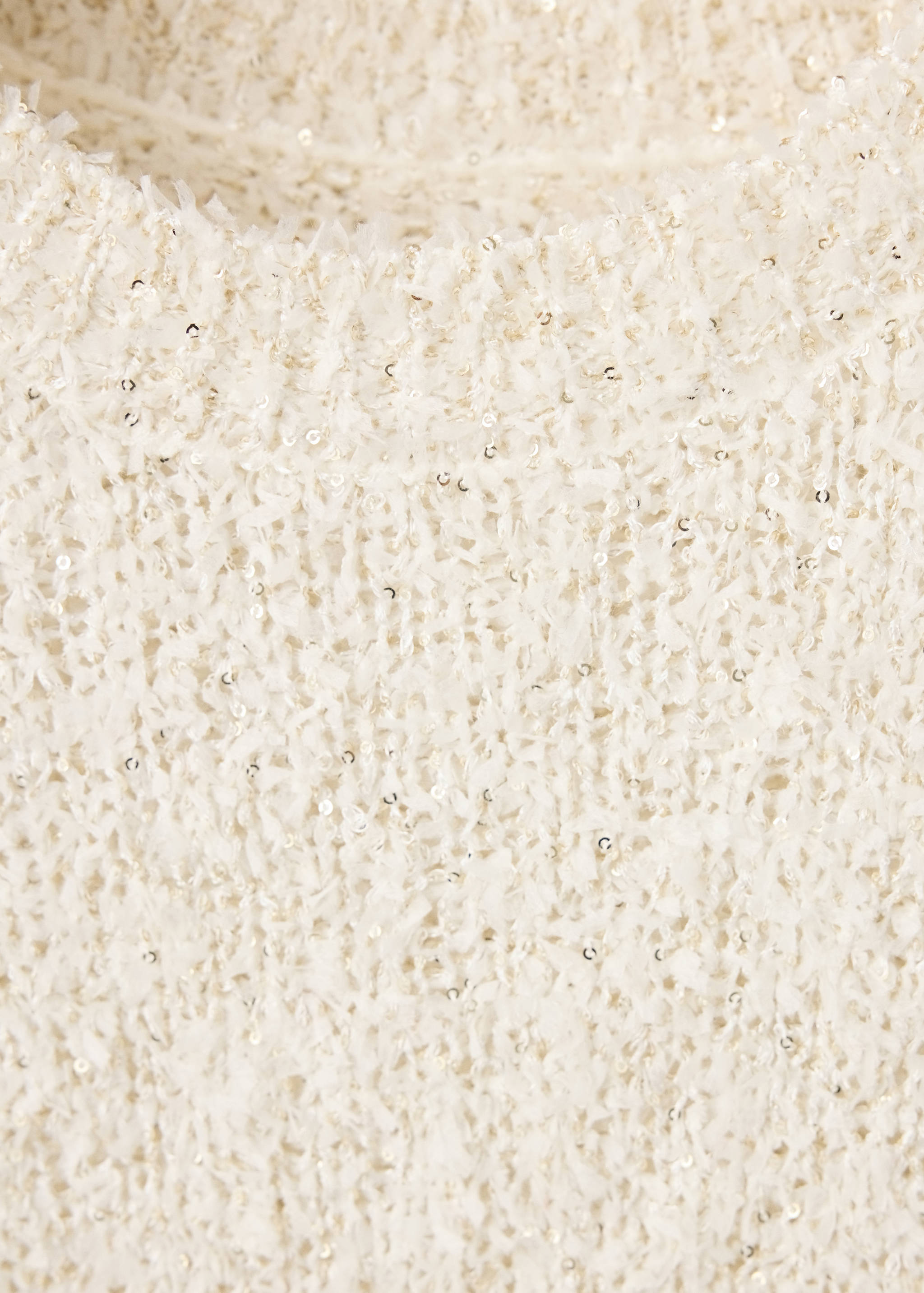 Primer plano de un jersey color crema de punto texturizado con pequeñas lentejuelas.