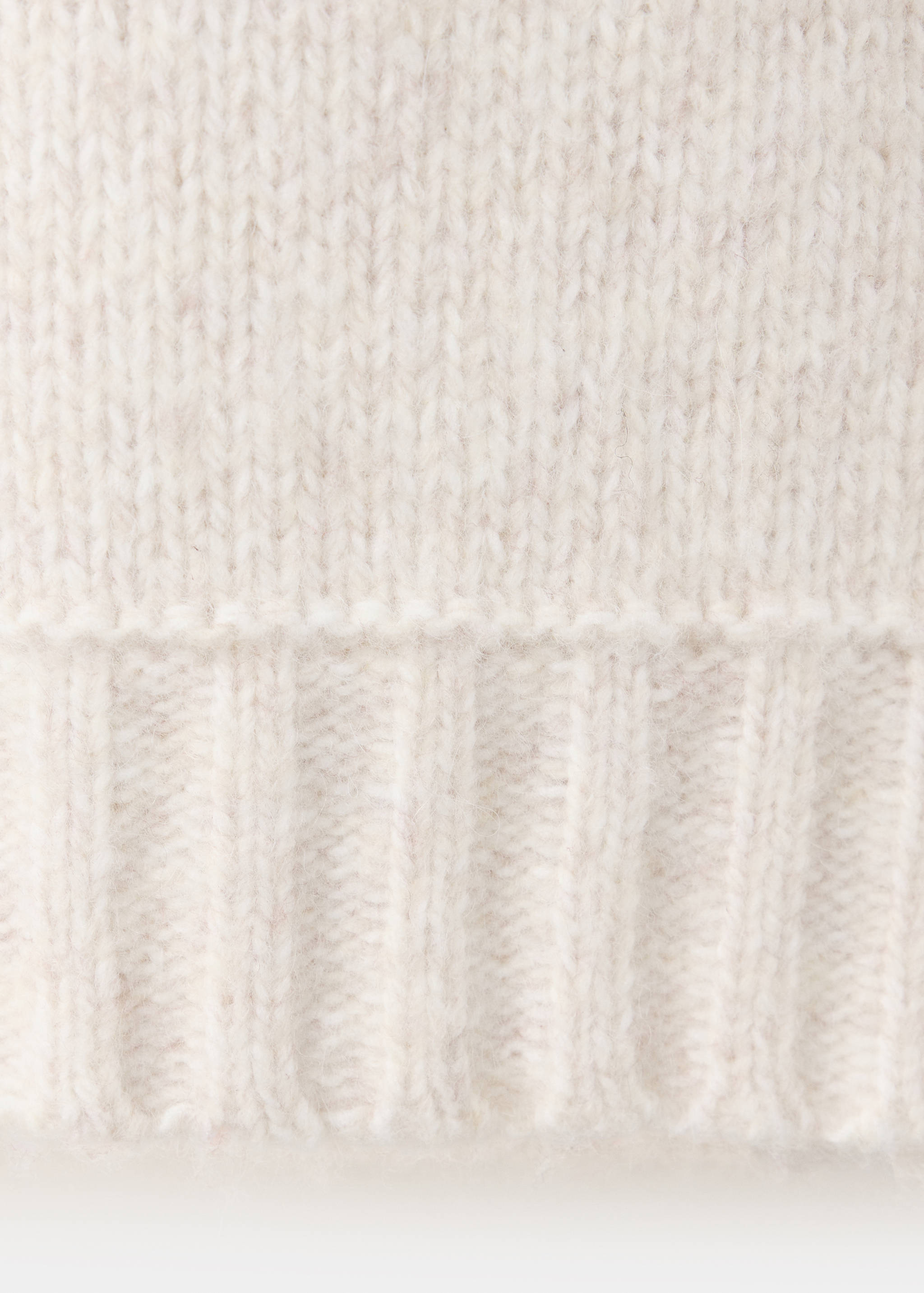 Close-up of the knit texture and ribbed hem on a beige jersey sweater.