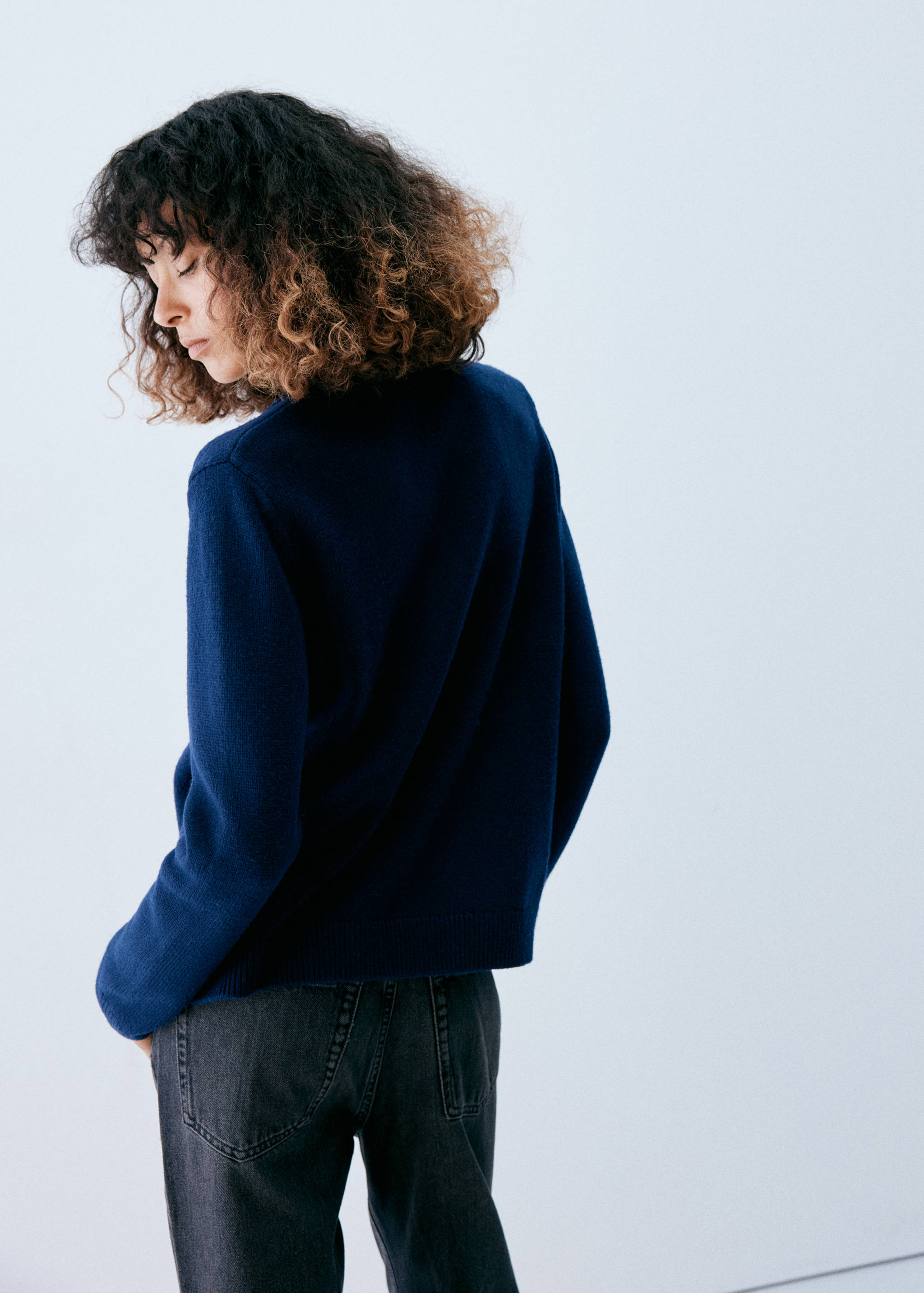 Dark blue knitted jumper, back view, paired with dark grey trousers.