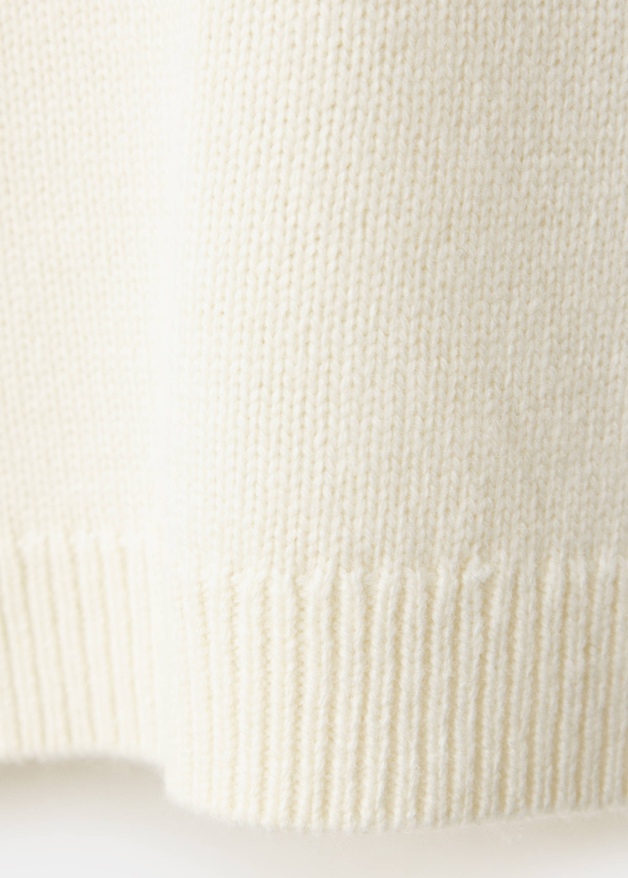 Close-up of the cream knit fabric and ribbed hem of a jersey.