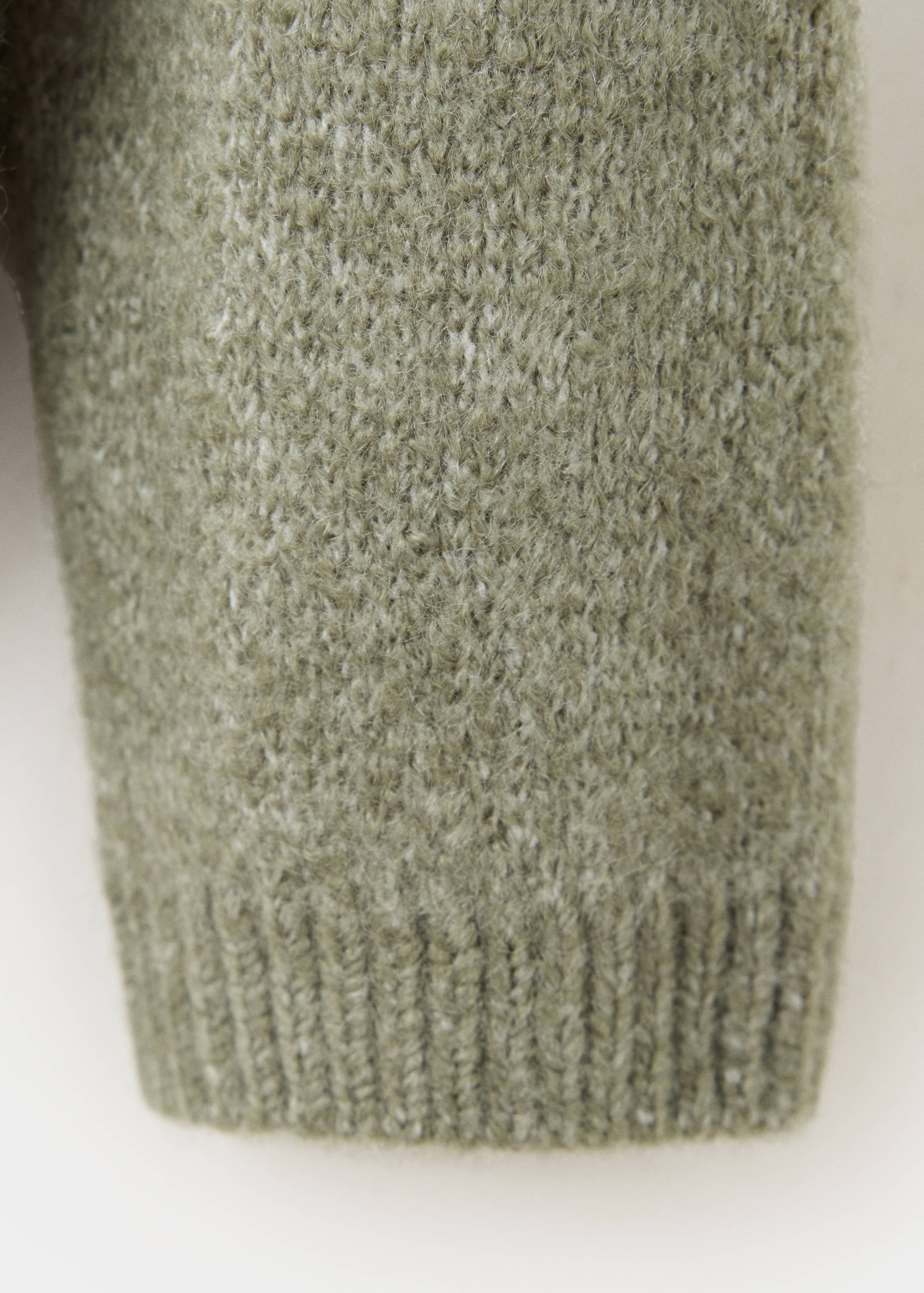 Green knit sweater fabric detail showing the fuzzy texture and ribbed cuff.