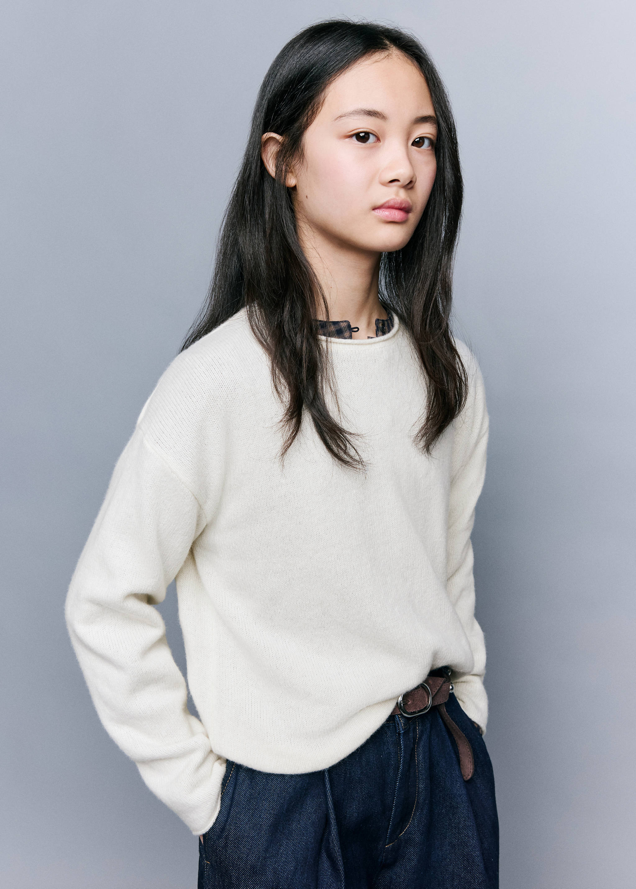 Cream round-neck knit sweater worn over a patterned shirt.
