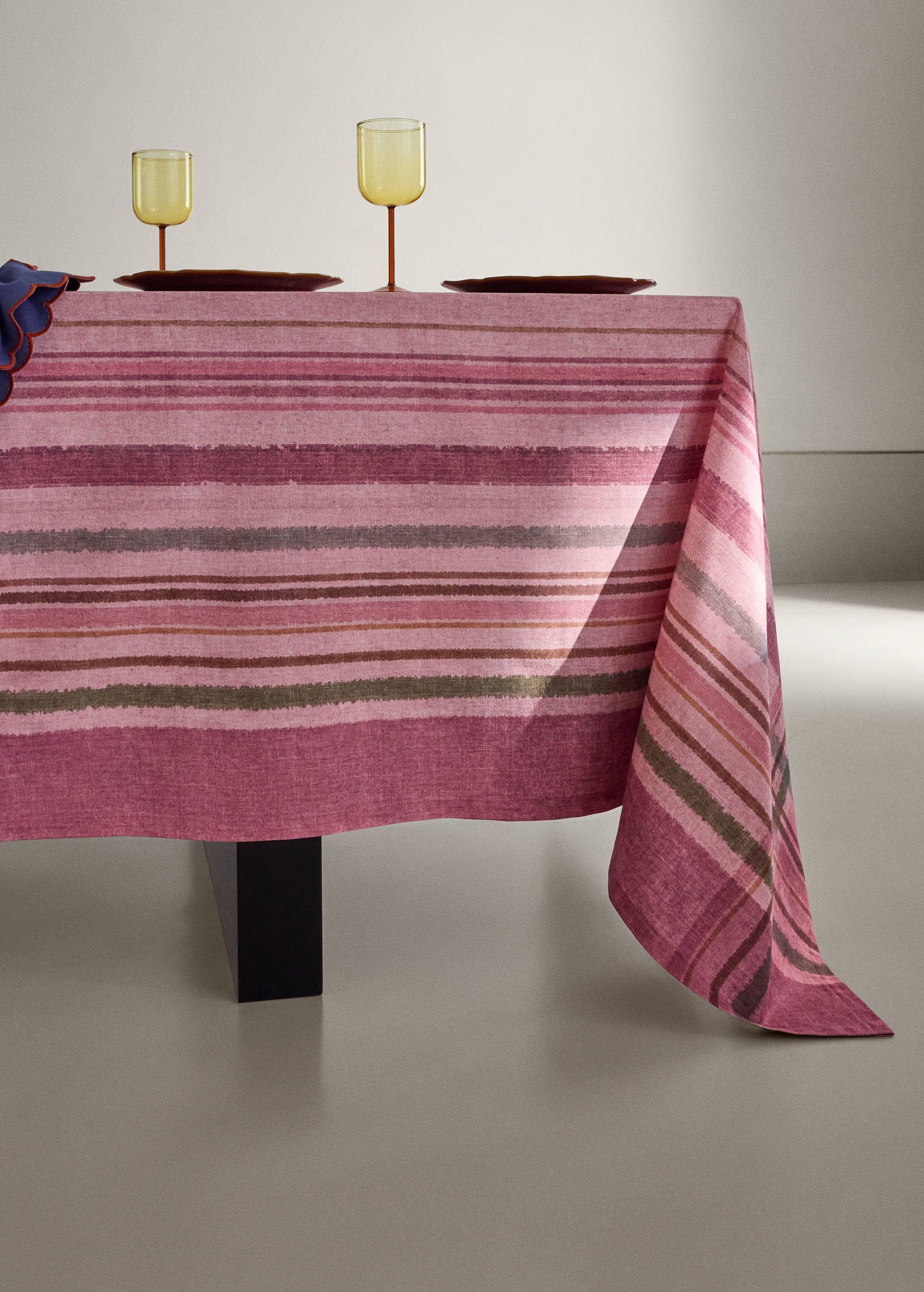 Pink striped tablecloth on a dining table with yellow-stemmed glasses.