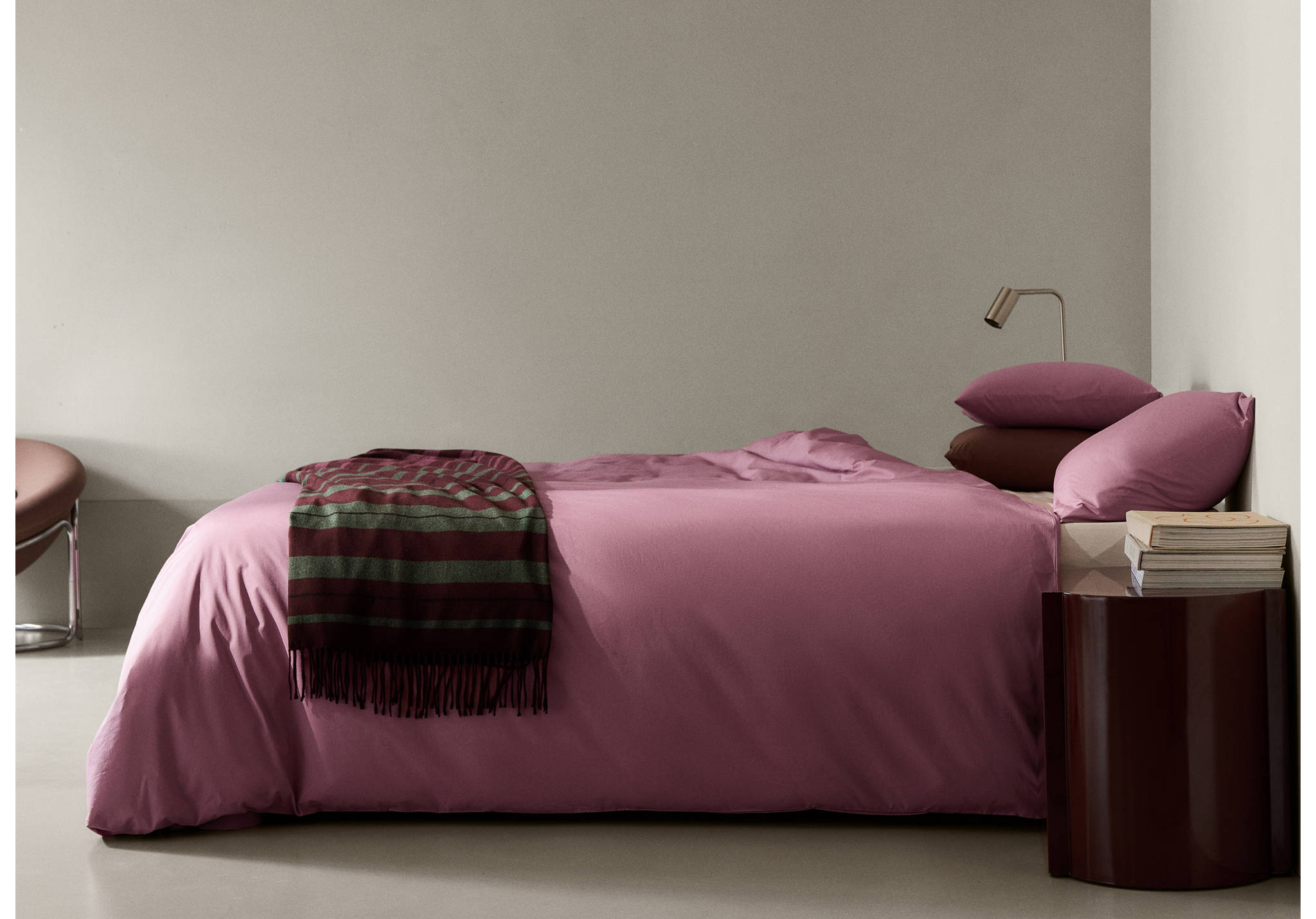 Mauve duvet cover on a made bed with a striped fringed throw blanket.