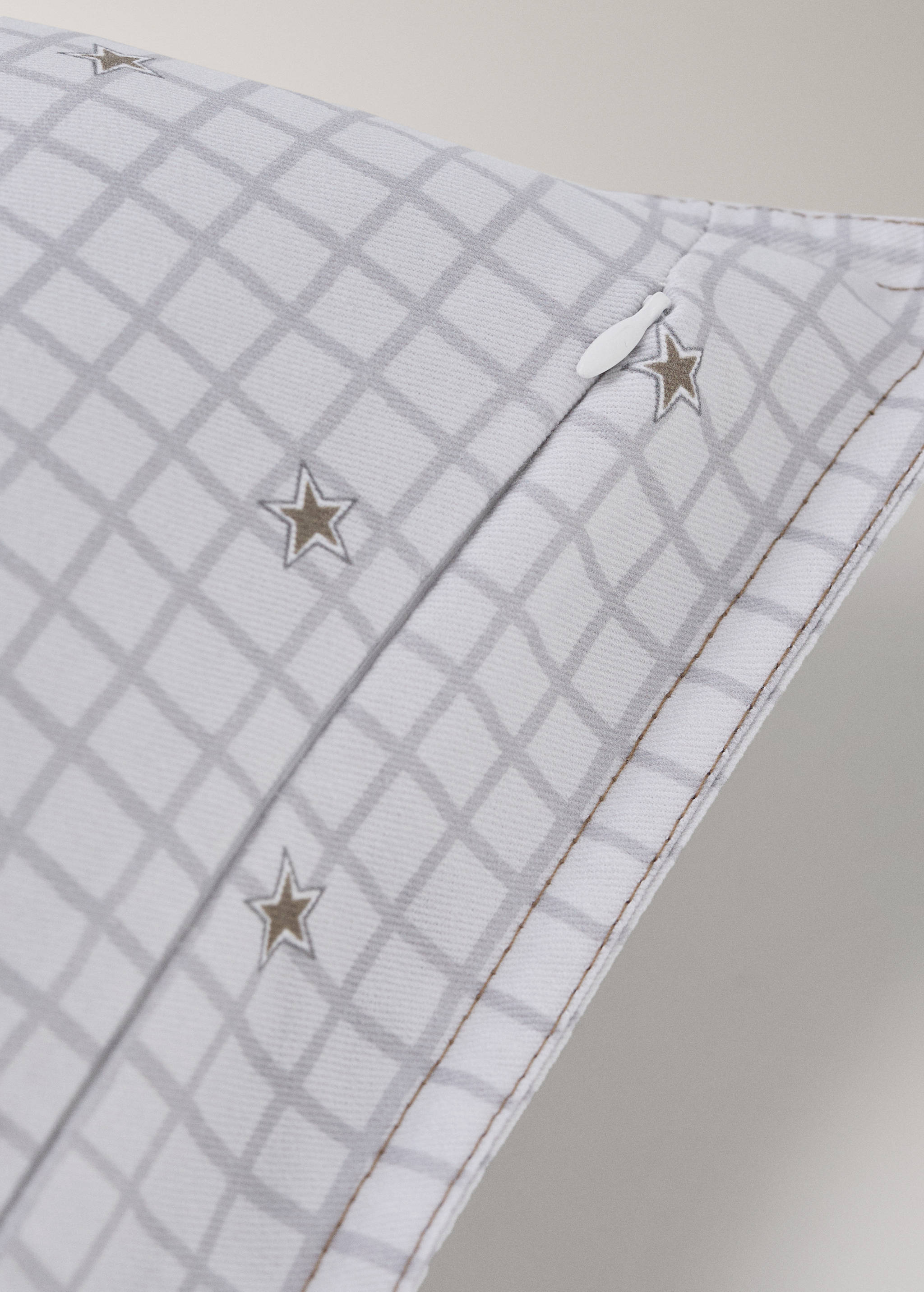 Close-up of a white cushion cover with a grey grid and star print.