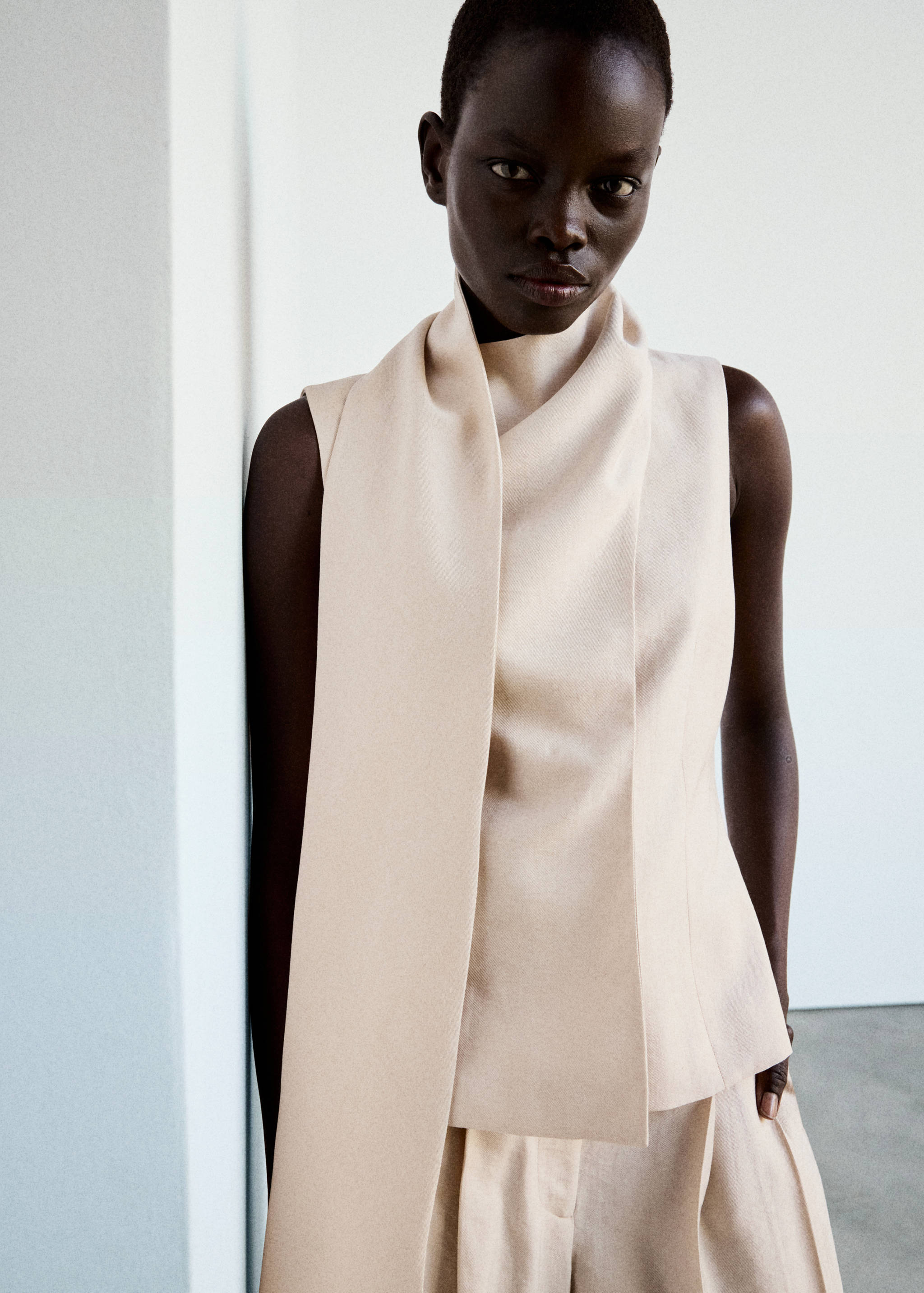 Sleeveless cream top with a high collar and draped front panel.