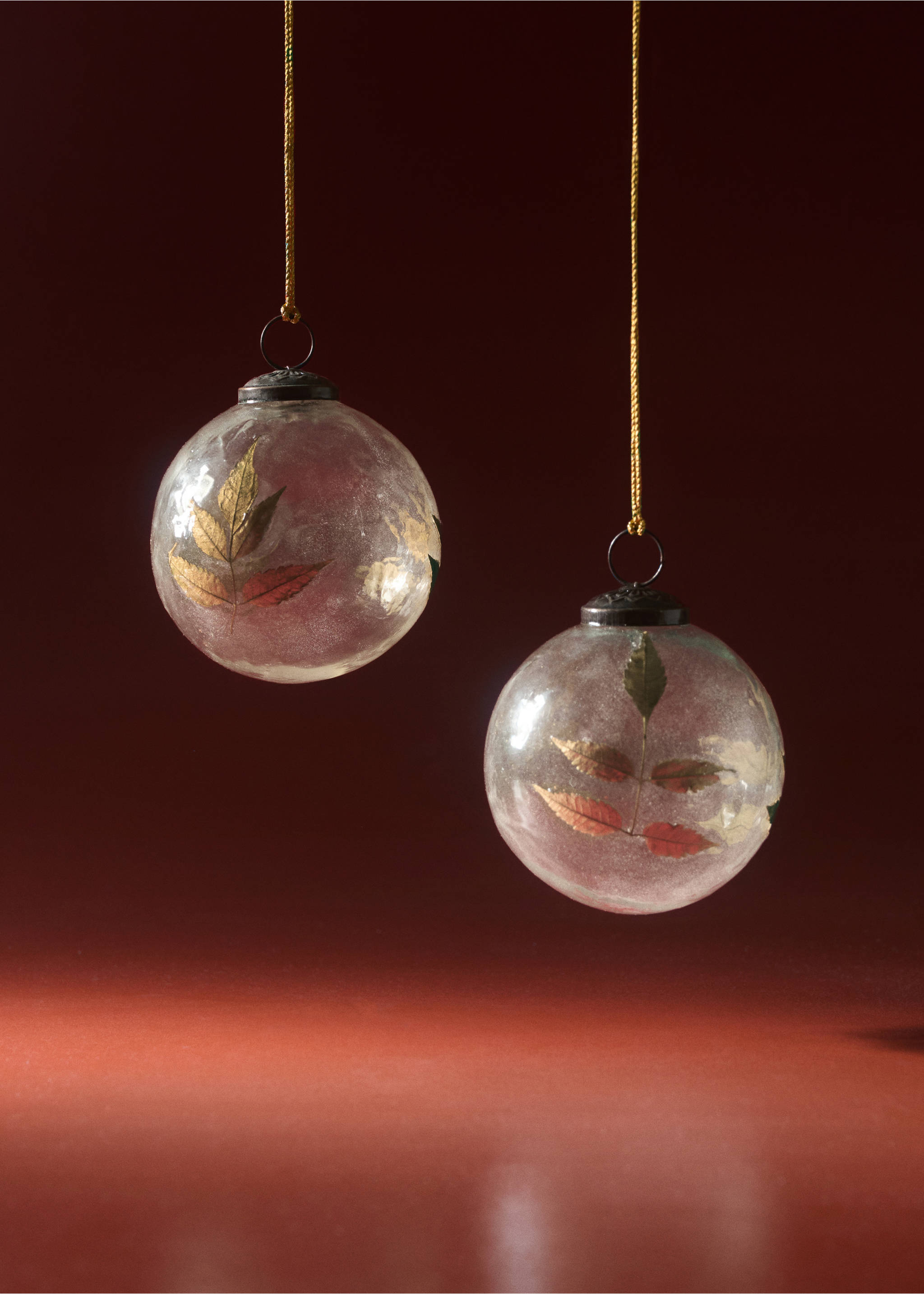 Two round glass Christmas ornaments containing pressed leaves, suspended by gold cords., Gold. Ref: 37016731-00.