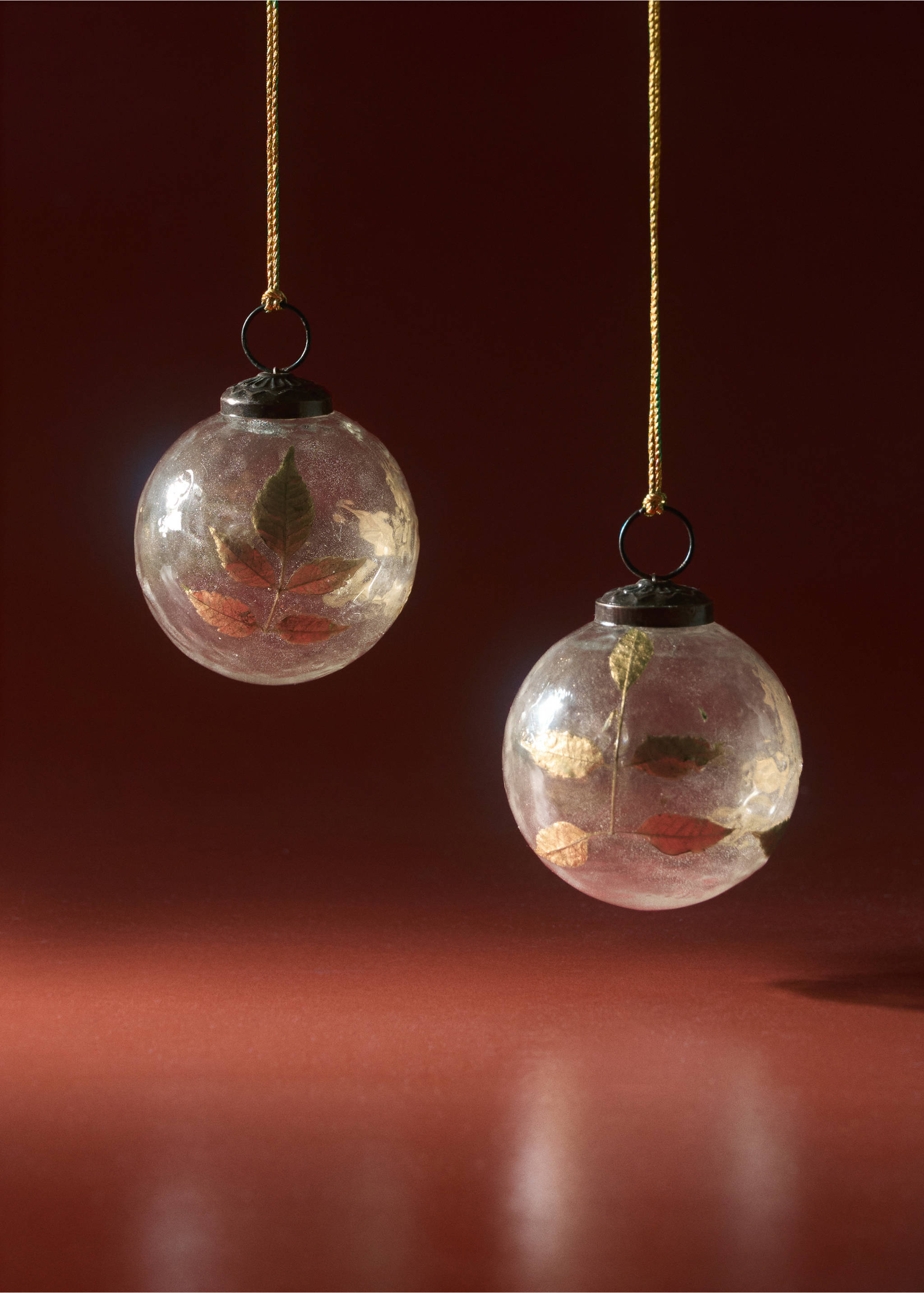 Two round glass Christmas ornaments with pressed autumn leaves inside, hanging by gold strings., Gold. Ref: 37016732-00.