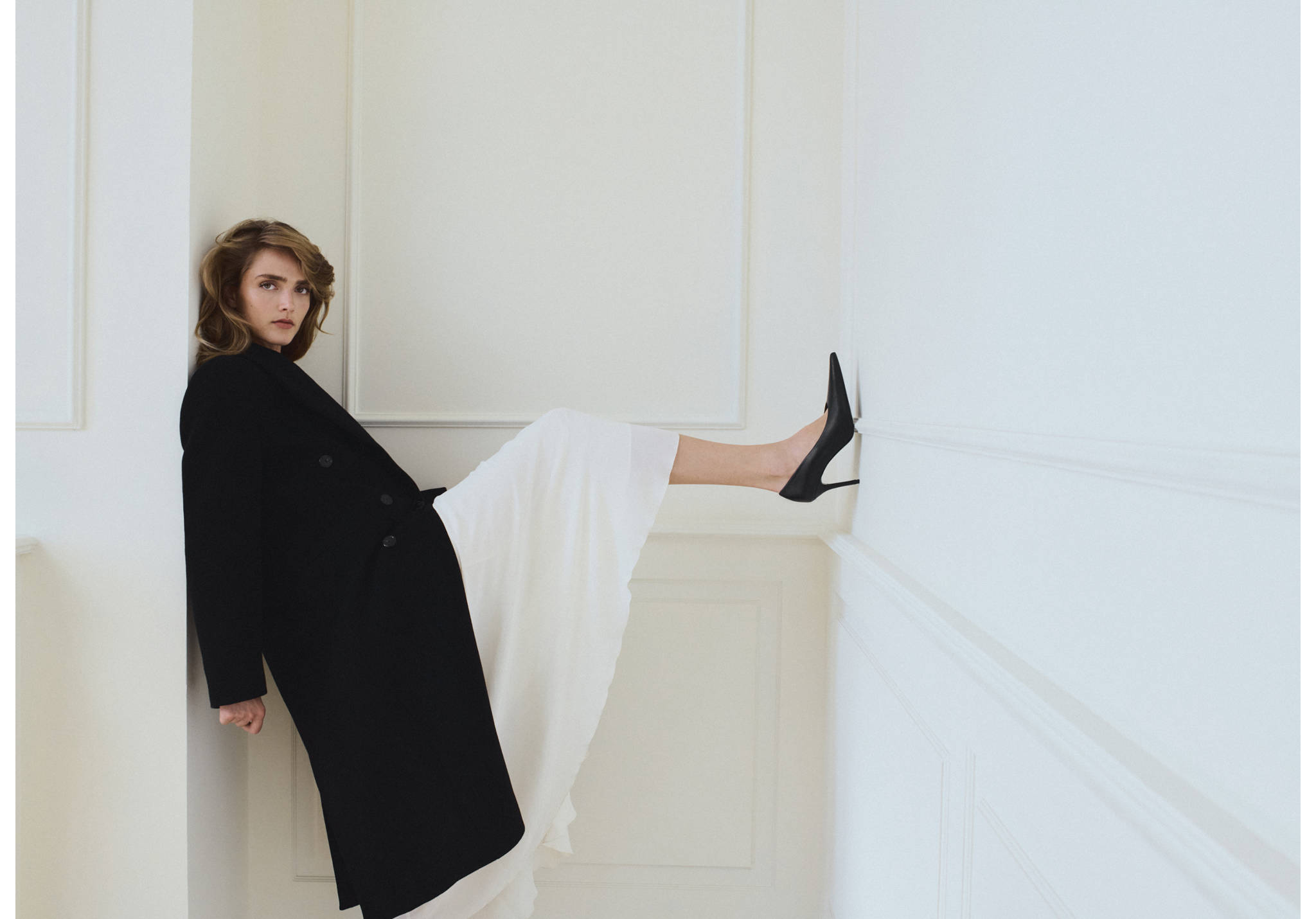 Long black coat worn with a white skirt and black stiletto shoes.