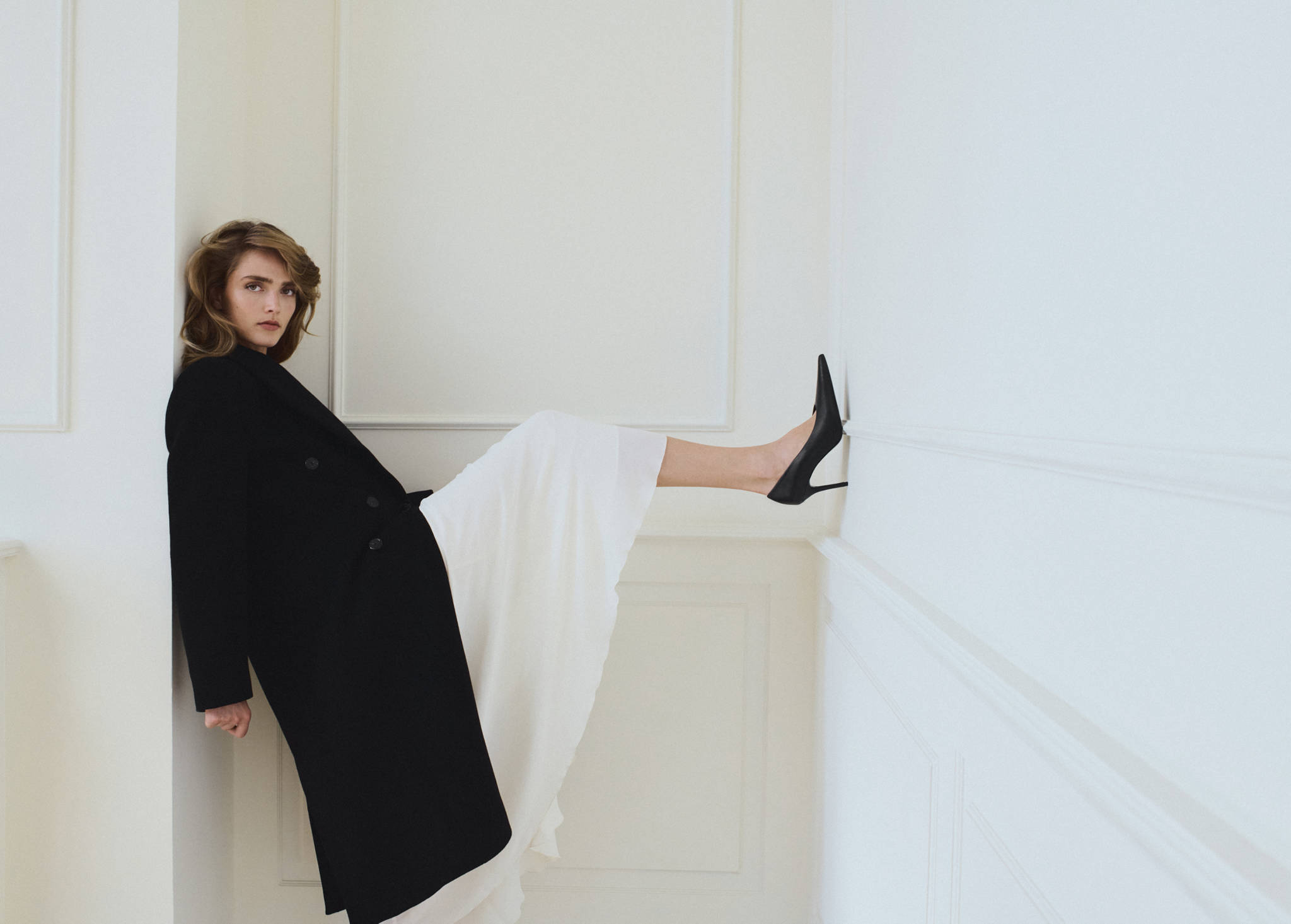 Long black coat worn with a white skirt and black stiletto shoes.