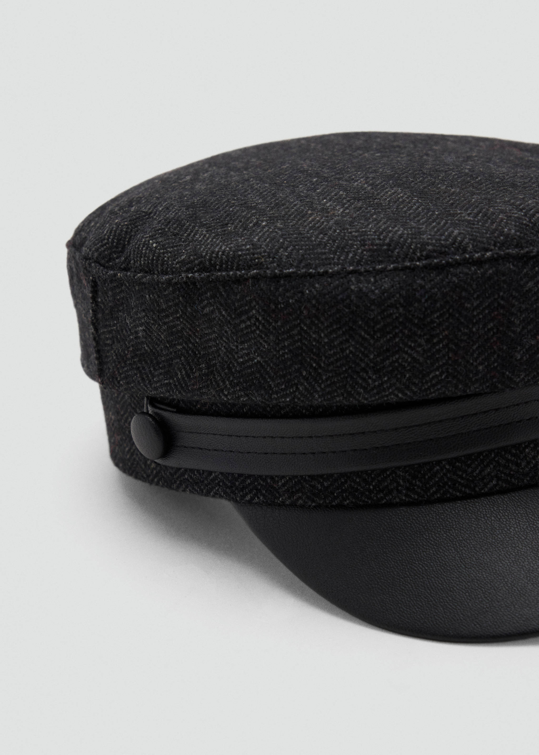 Close-up of a dark grey herringbone cap with a black visor.