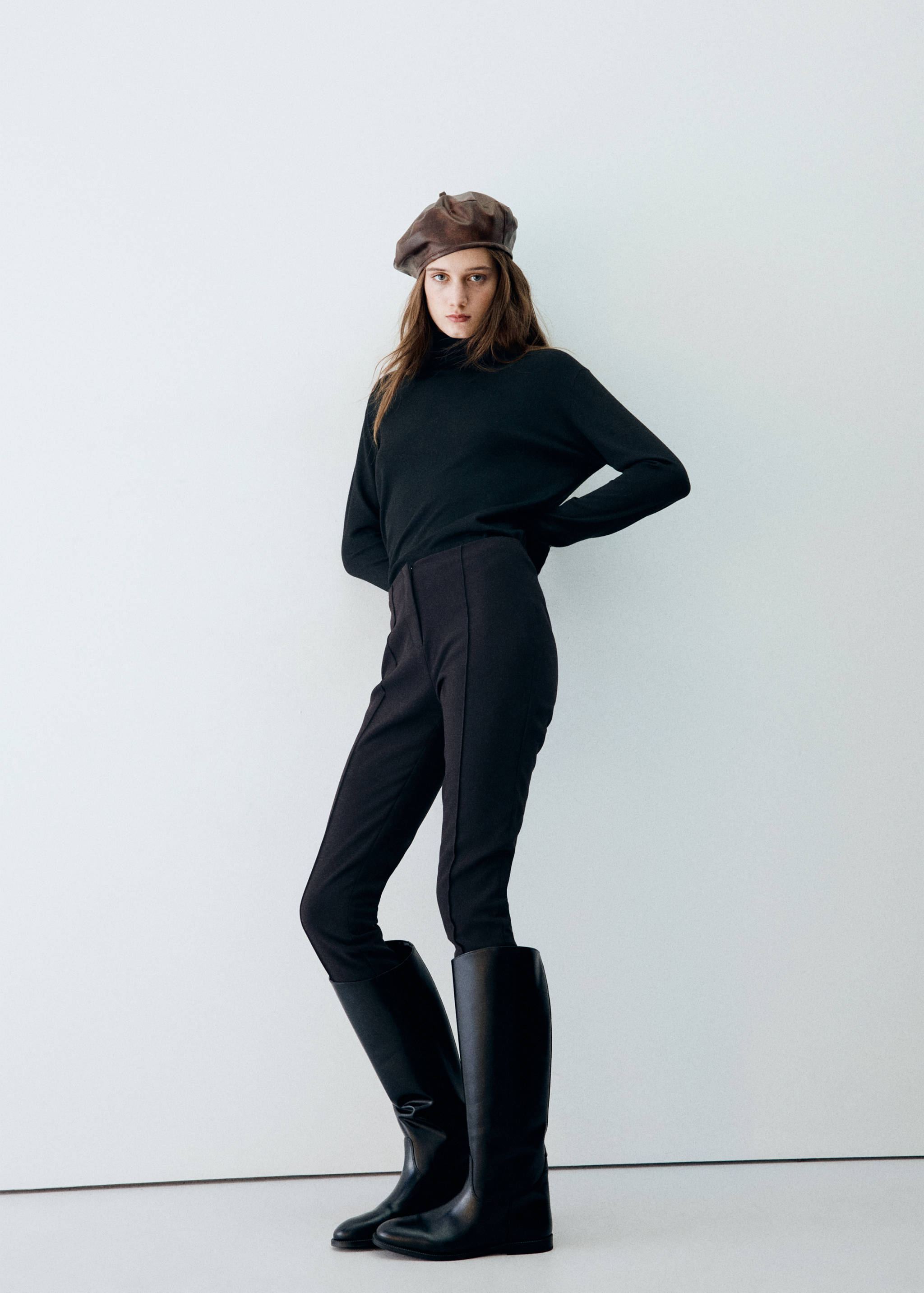 Brown leather beret worn by a model in a black top and trousers.