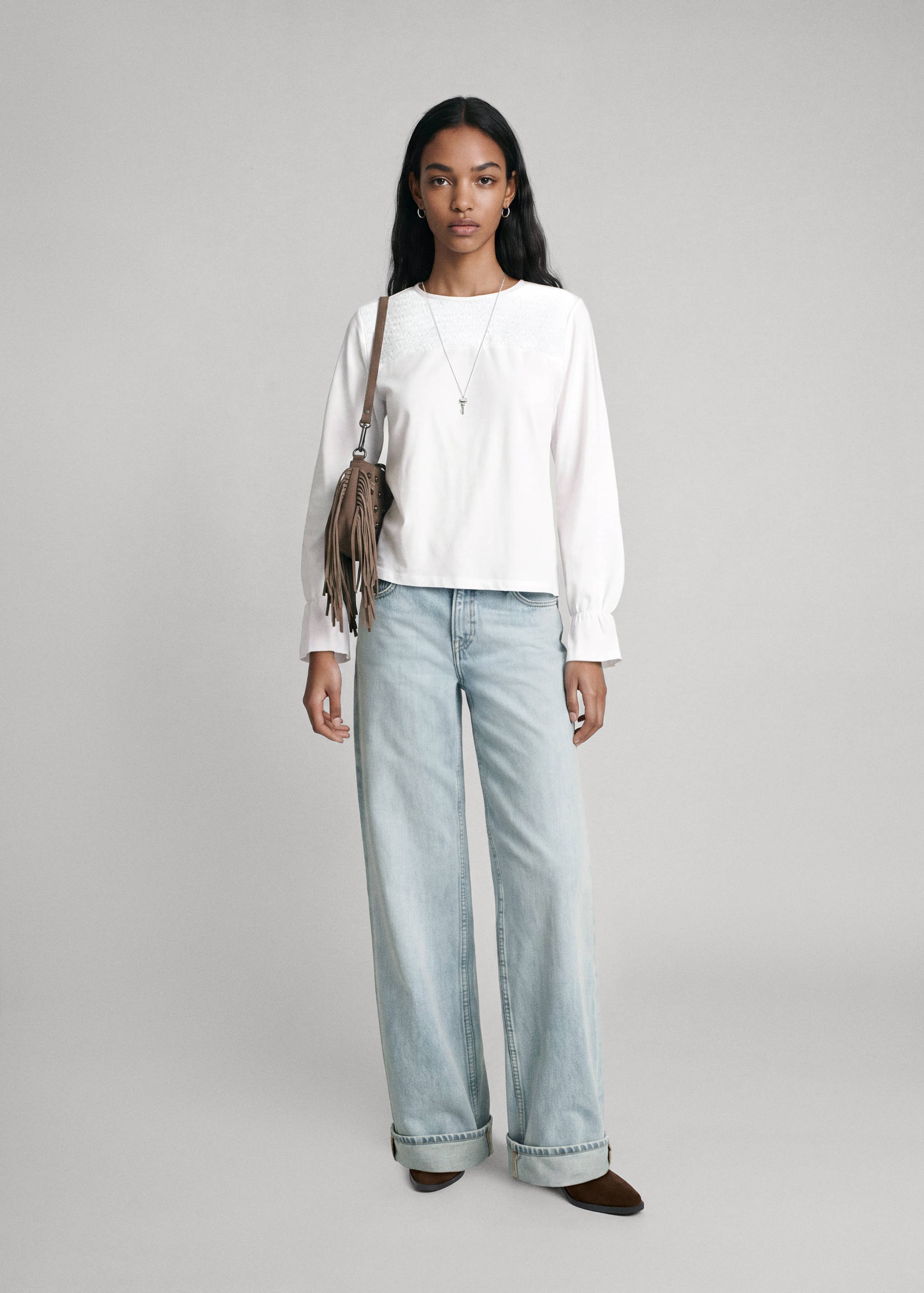 White long-sleeved t-shirt with embroidered detail, paired with light blue wide-leg jeans.