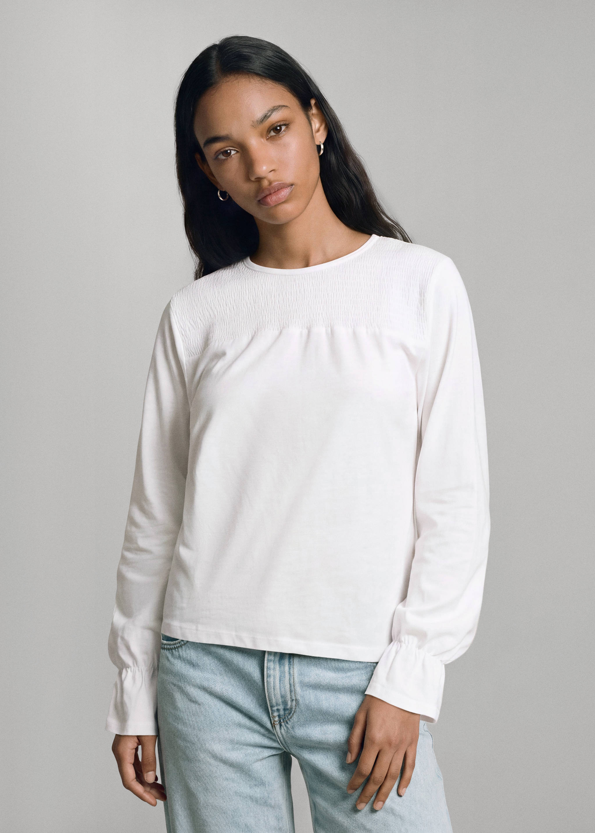 White long-sleeved t-shirt with smocked yoke and ruffled cuffs.
