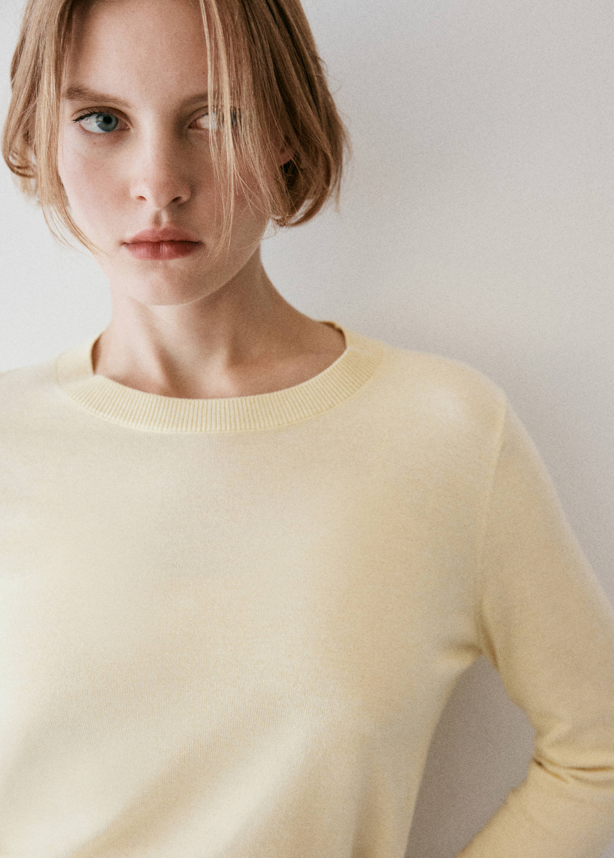 Close-up of a pastel yellow jersey sweater with a round ribbed neckline.