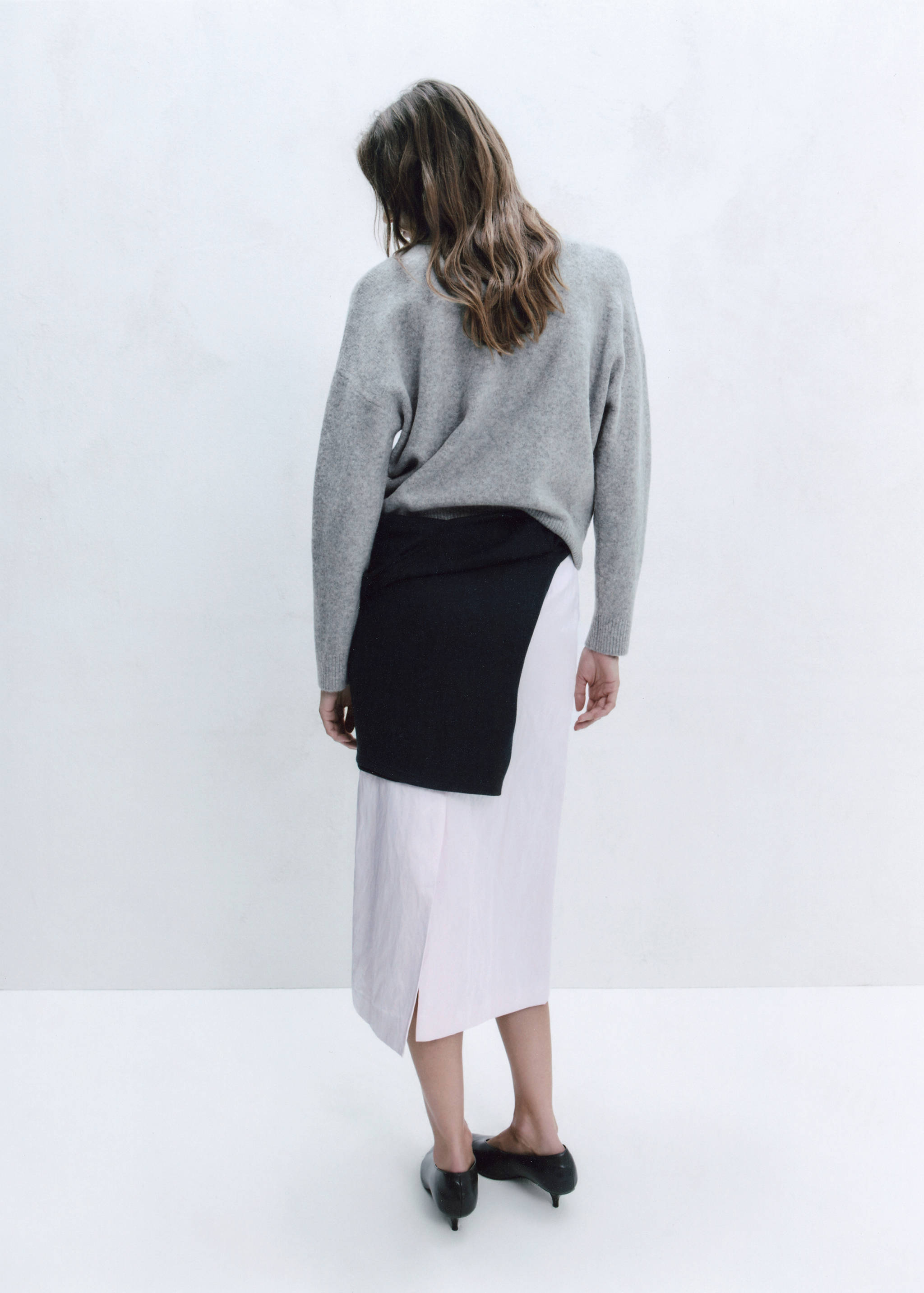 Back view of a grey knitted sweater worn with a pink midi skirt.