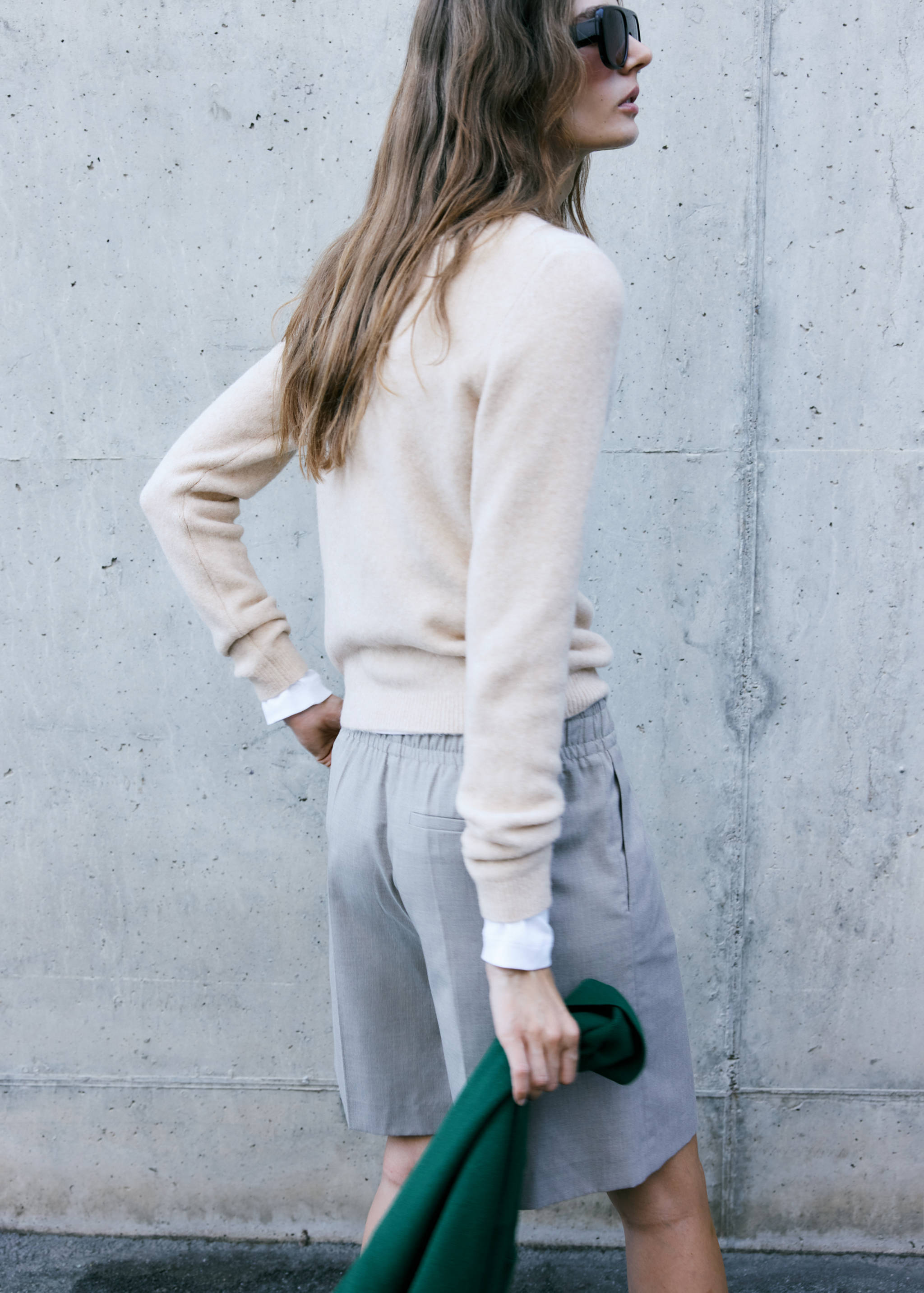 Cream knit jersey viewed from behind, paired with grey trousers.