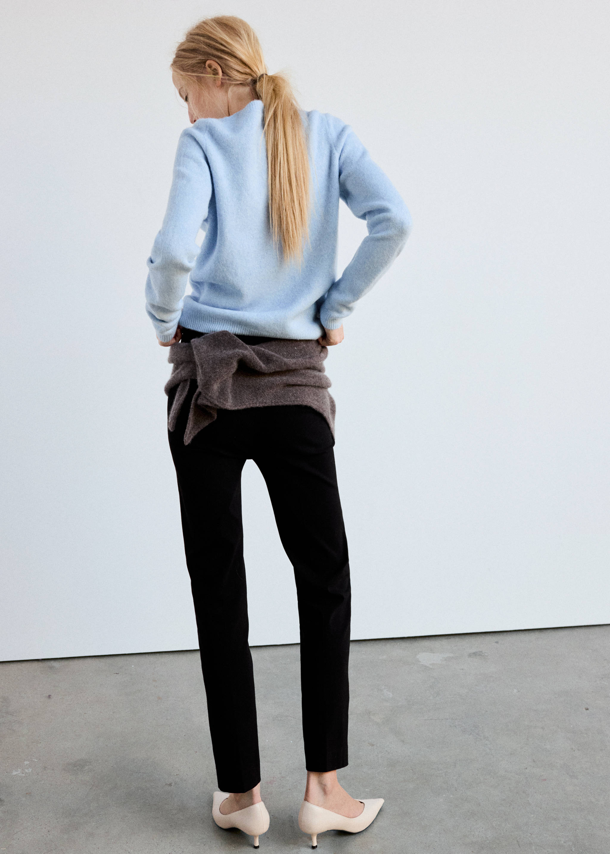 Back view of a light blue knitted jersey worn with black trousers.