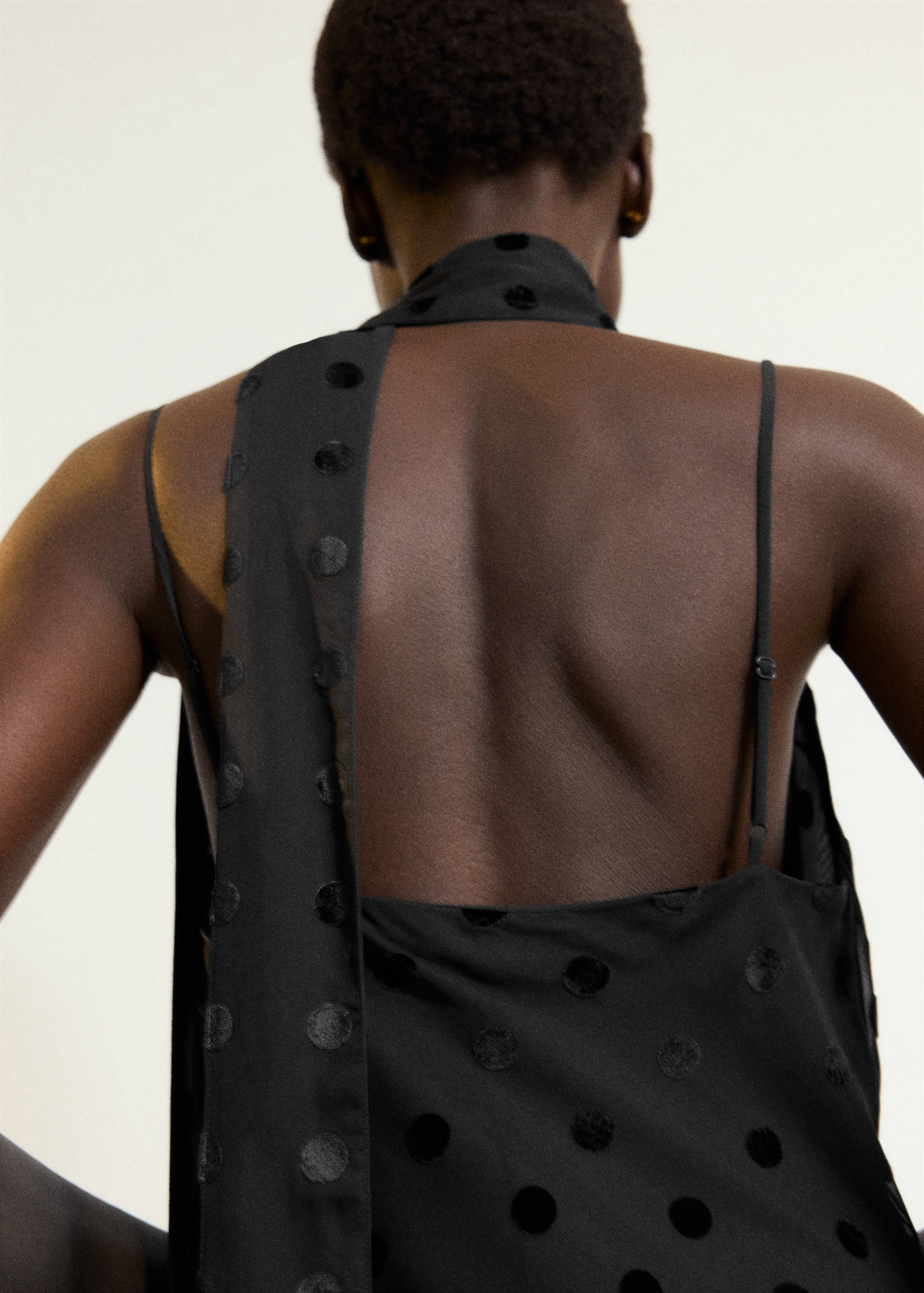 Black dotted flock dress featuring a draped neck scarf detail, back view.
