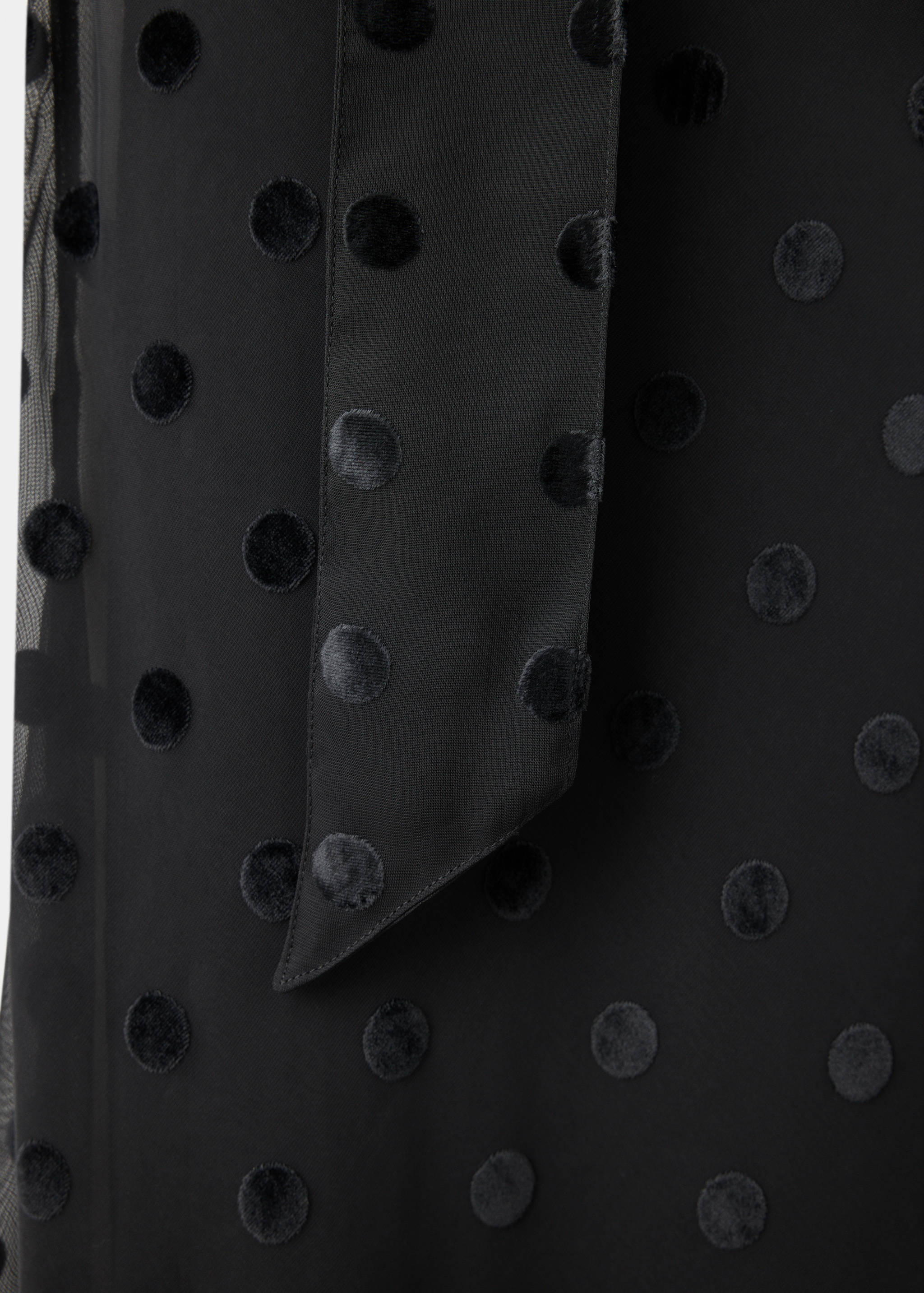 Close-up of a black dress fabric with velvet polka dots and a tie detail.