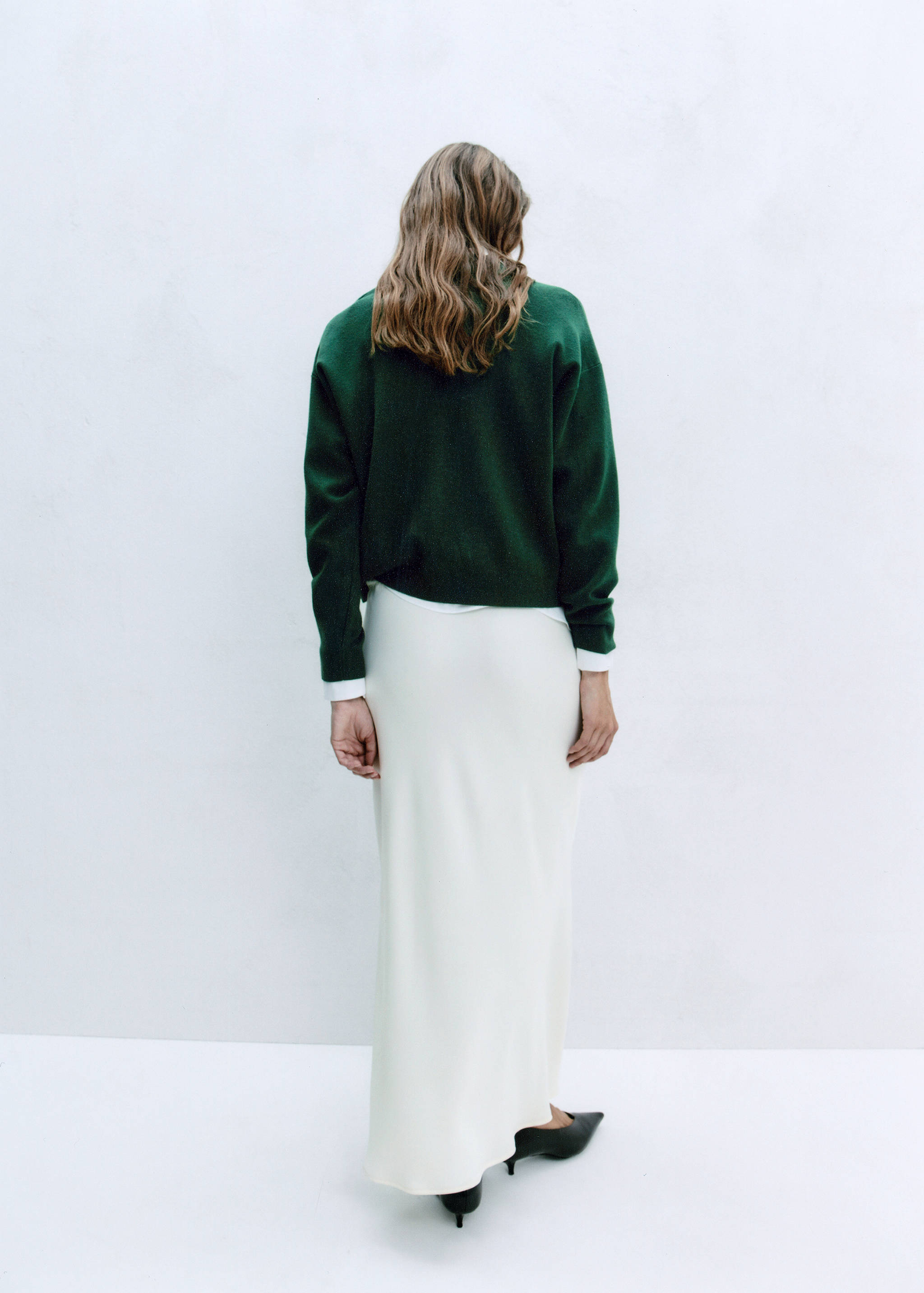 Dark green knitted jumper seen from the back, worn over a white shirt.