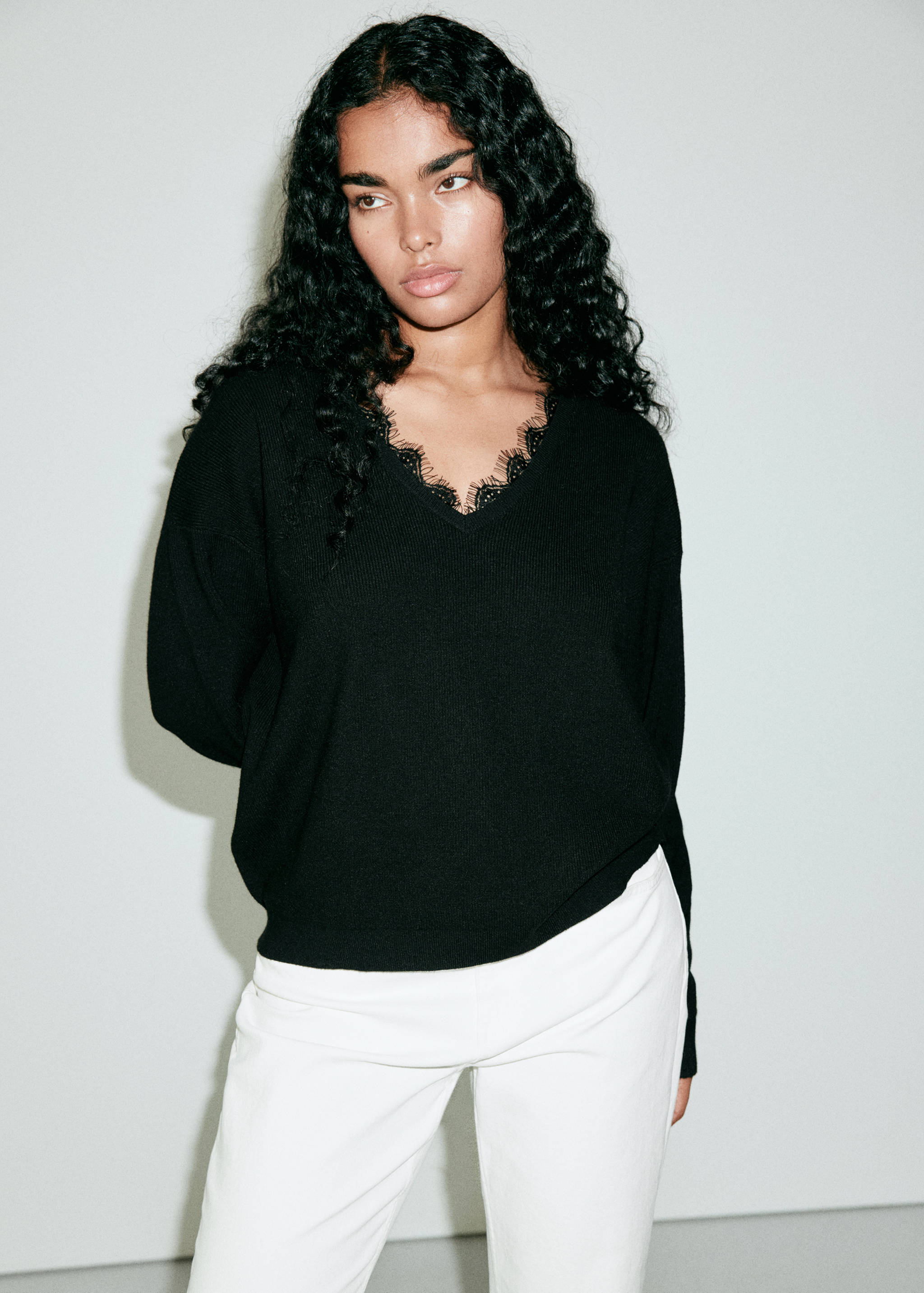 Black knitted V-neck jersey with delicate lace trim worn with white trousers.