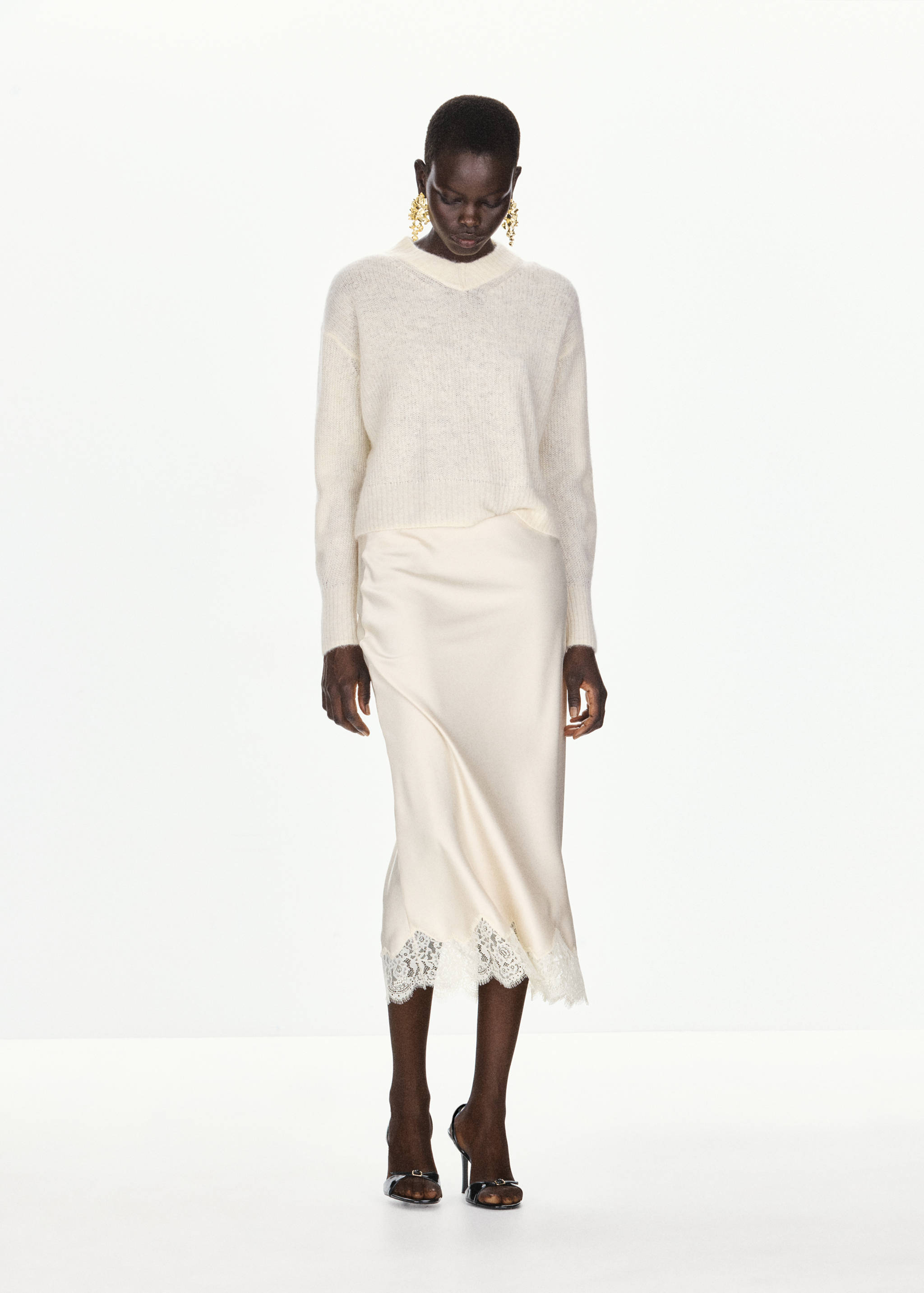 Cream V-neck knit sweater worn with a matching midi skirt with lace trim.
