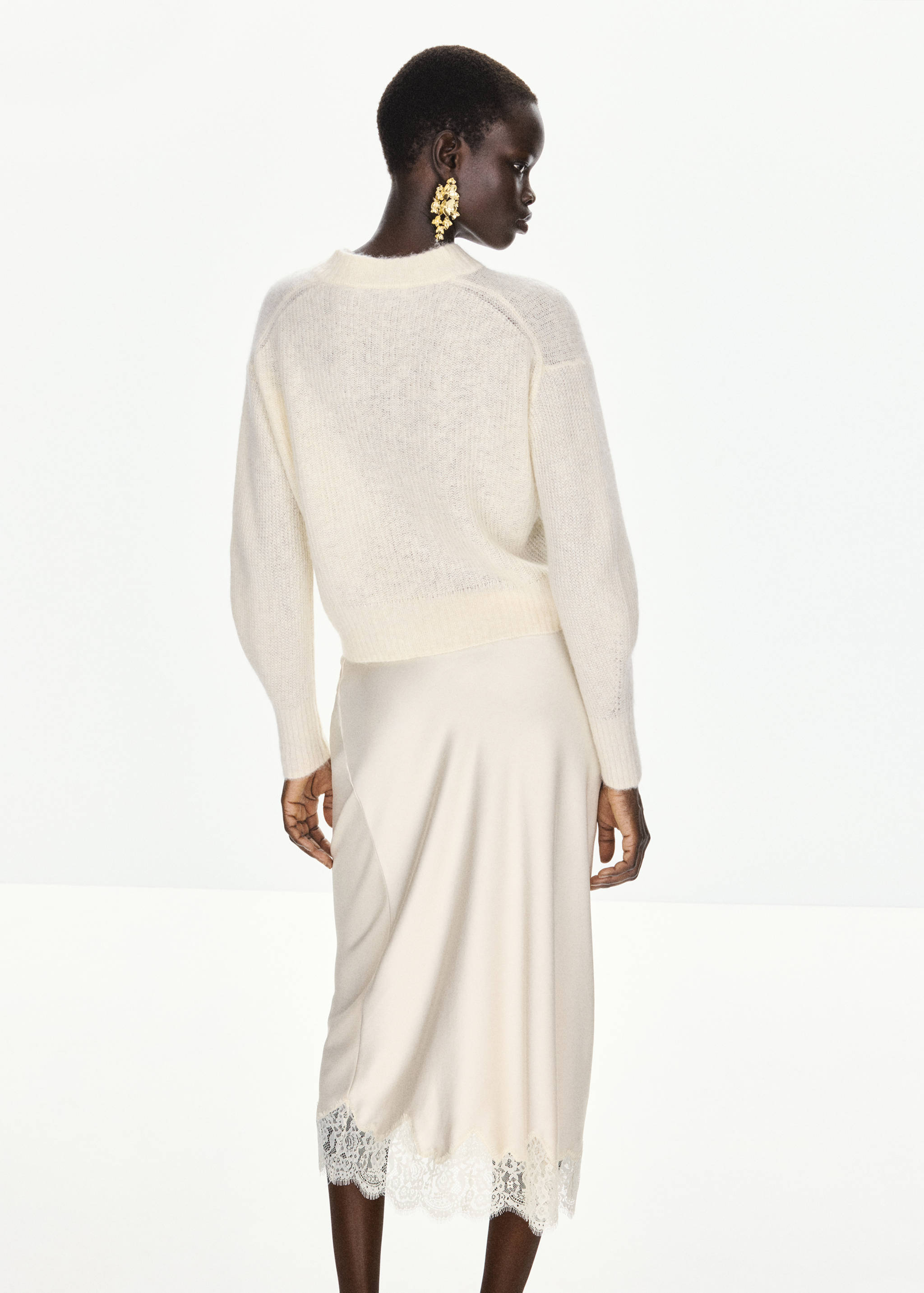 Cream knit sweater seen from the back, paired with a satin skirt.