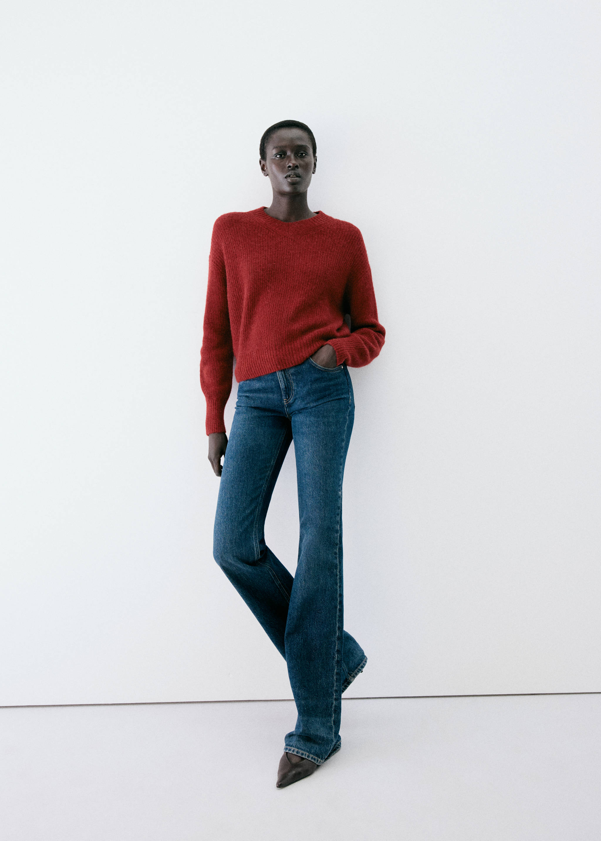 Dark red knitted jumper with a round neckline, worn with blue denim trousers.