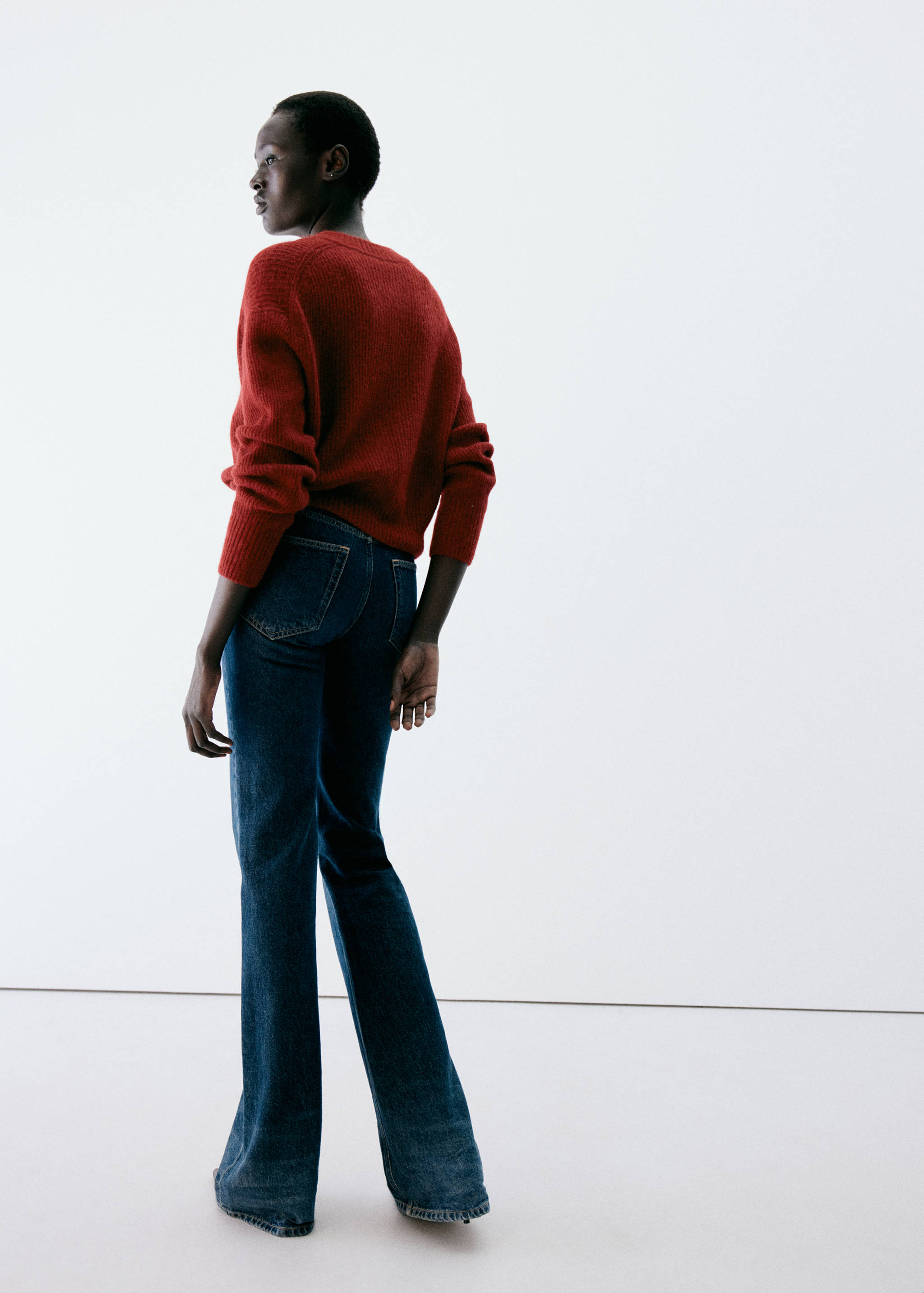Rust red knitted jumper with a back view, worn with blue denim trousers.