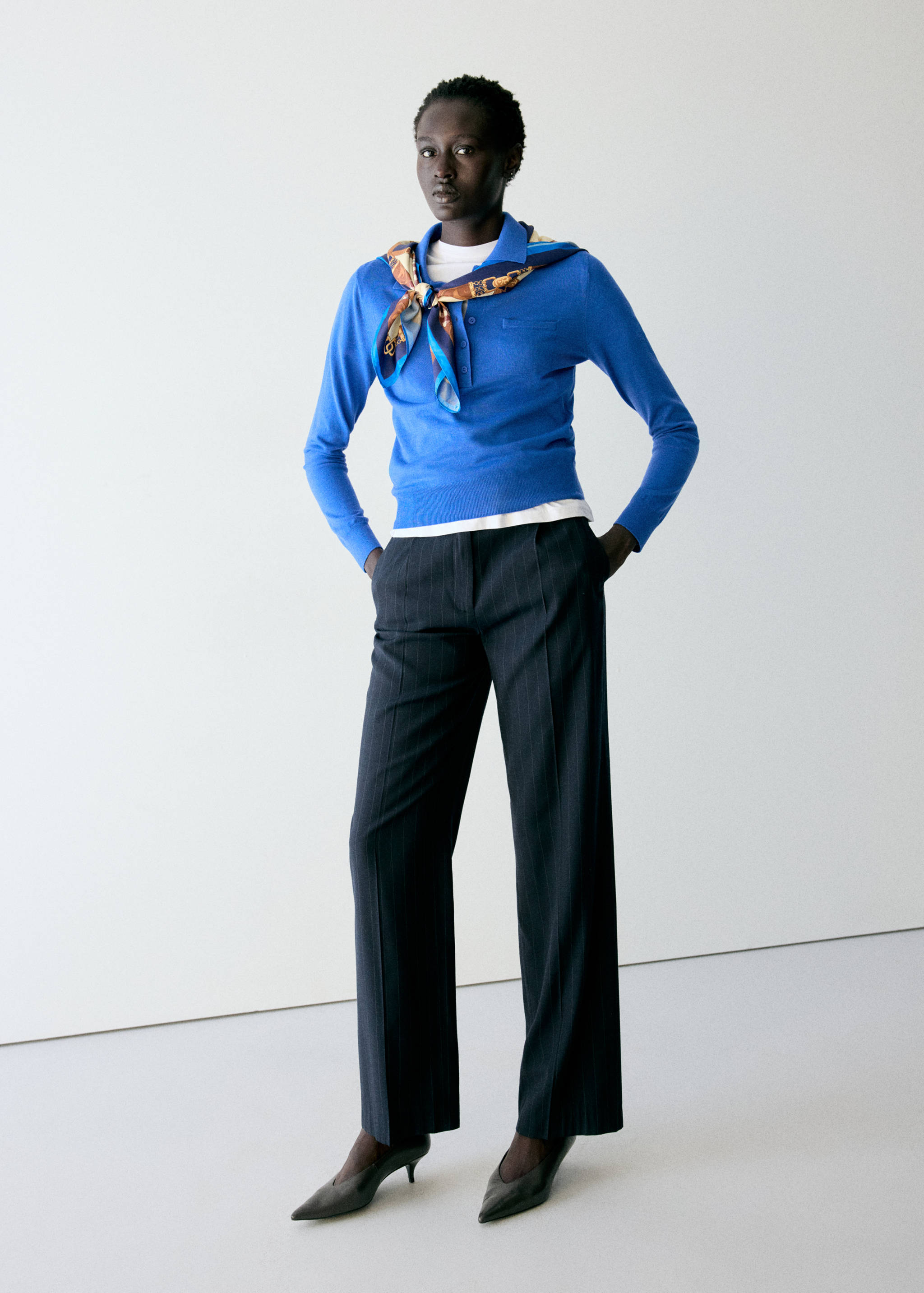 Blue knit polo jersey with a button placket, layered over a white t-shirt and styled with trousers.