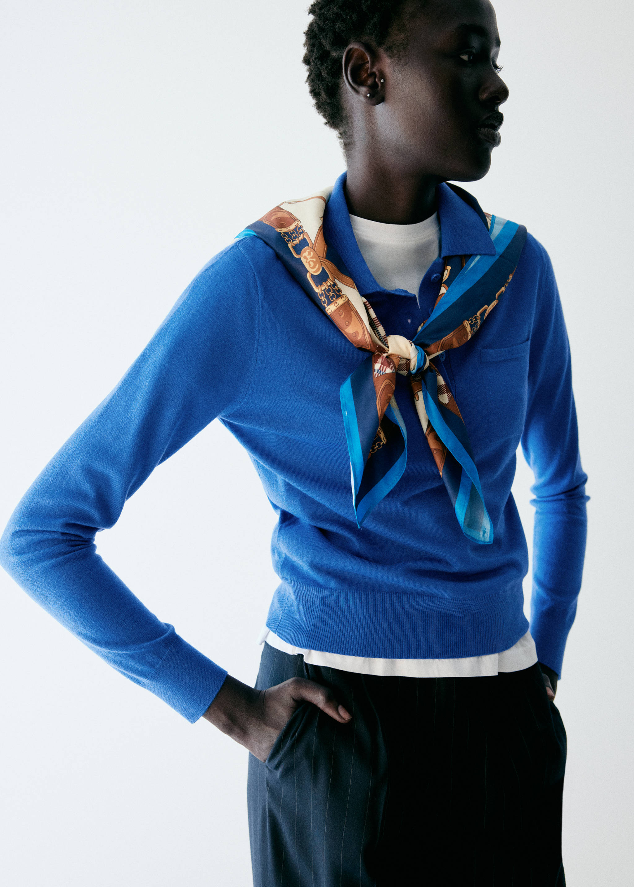 Vibrant blue knit polo sweater with a collar and long sleeves, layered with a patterned scarf.