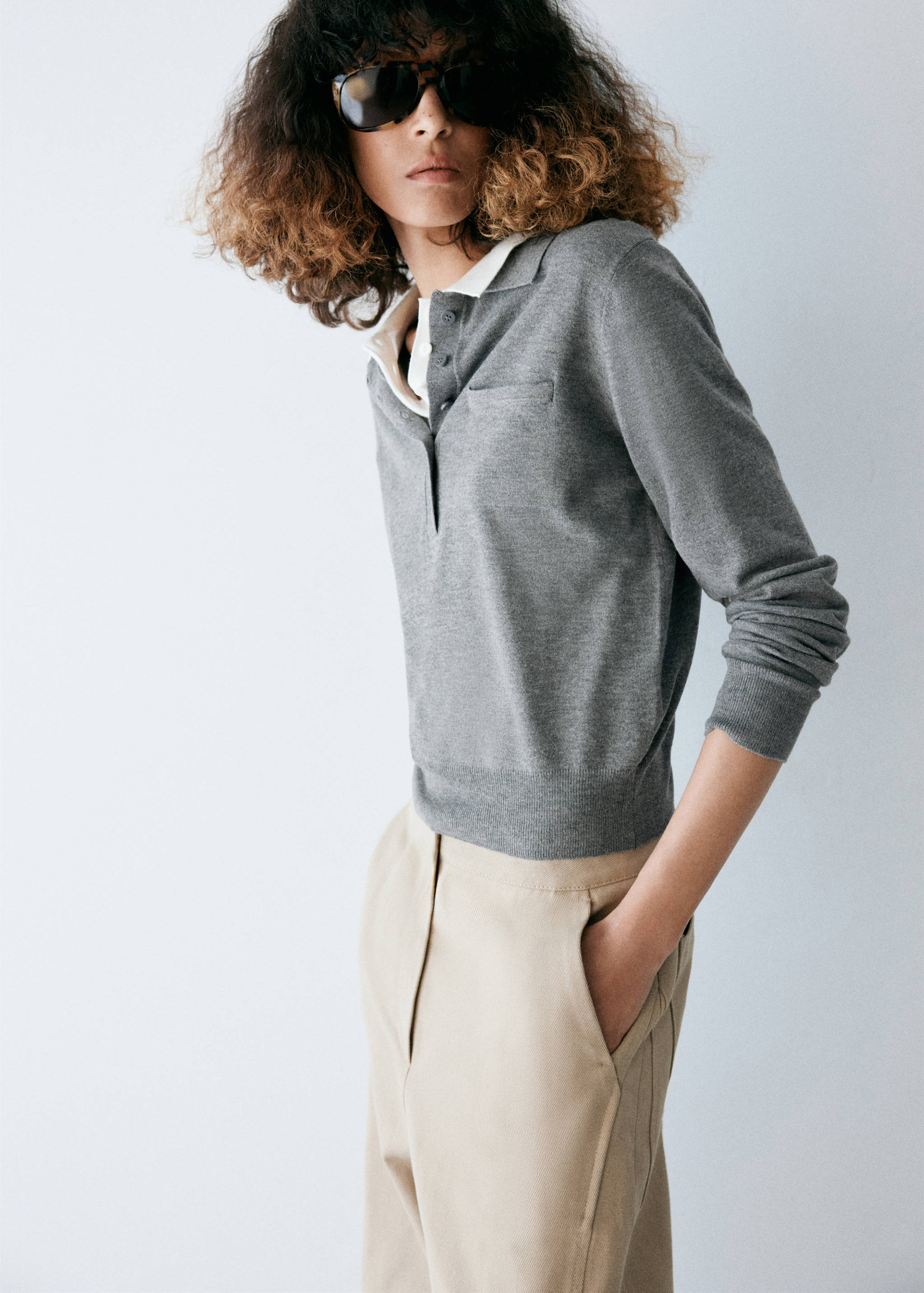 Grey knitted jumper with a polo collar, buttoned placket, and layered white shirt.