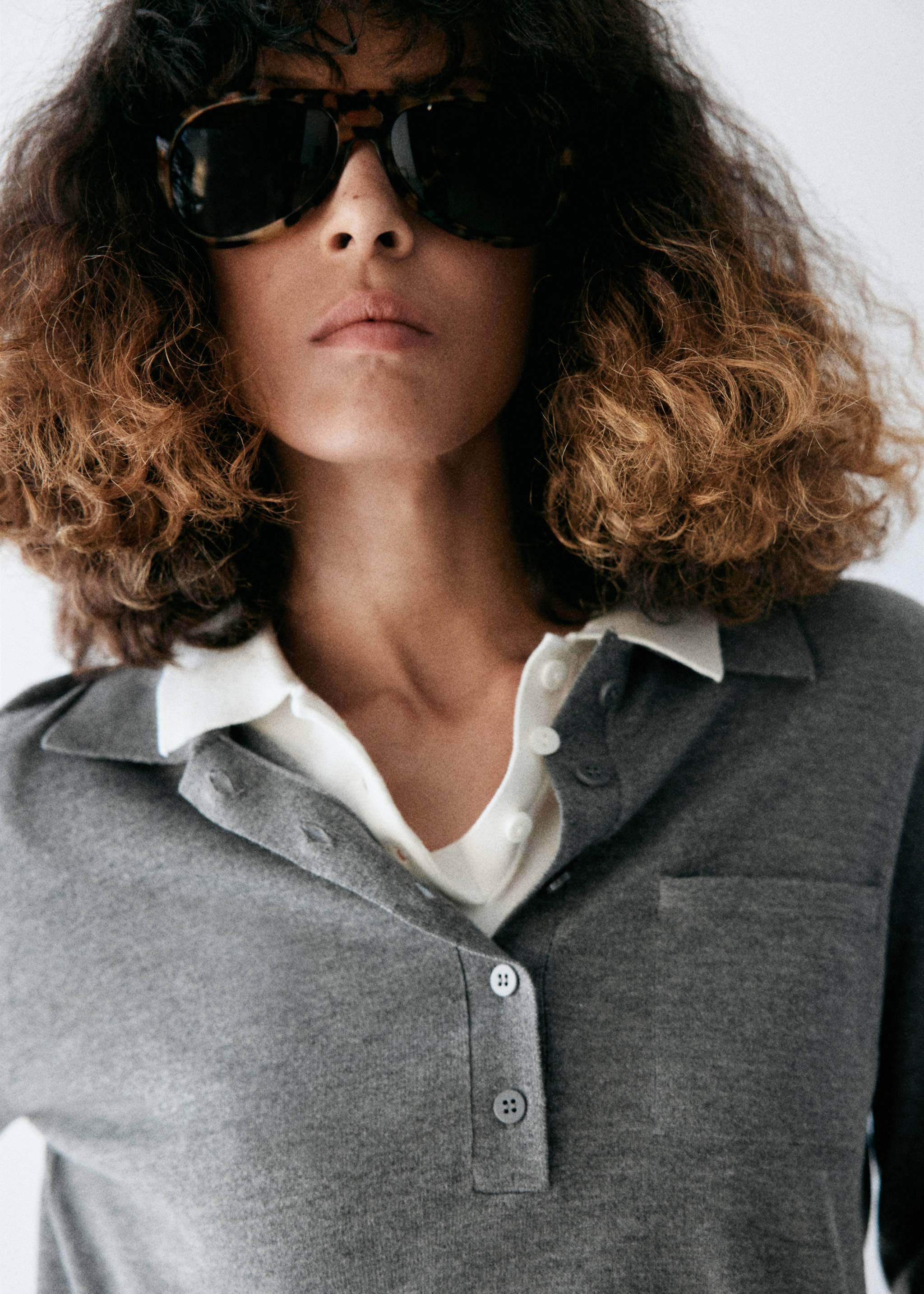 Close-up of a grey knitted jersey with a polo collar and layered white shirt.