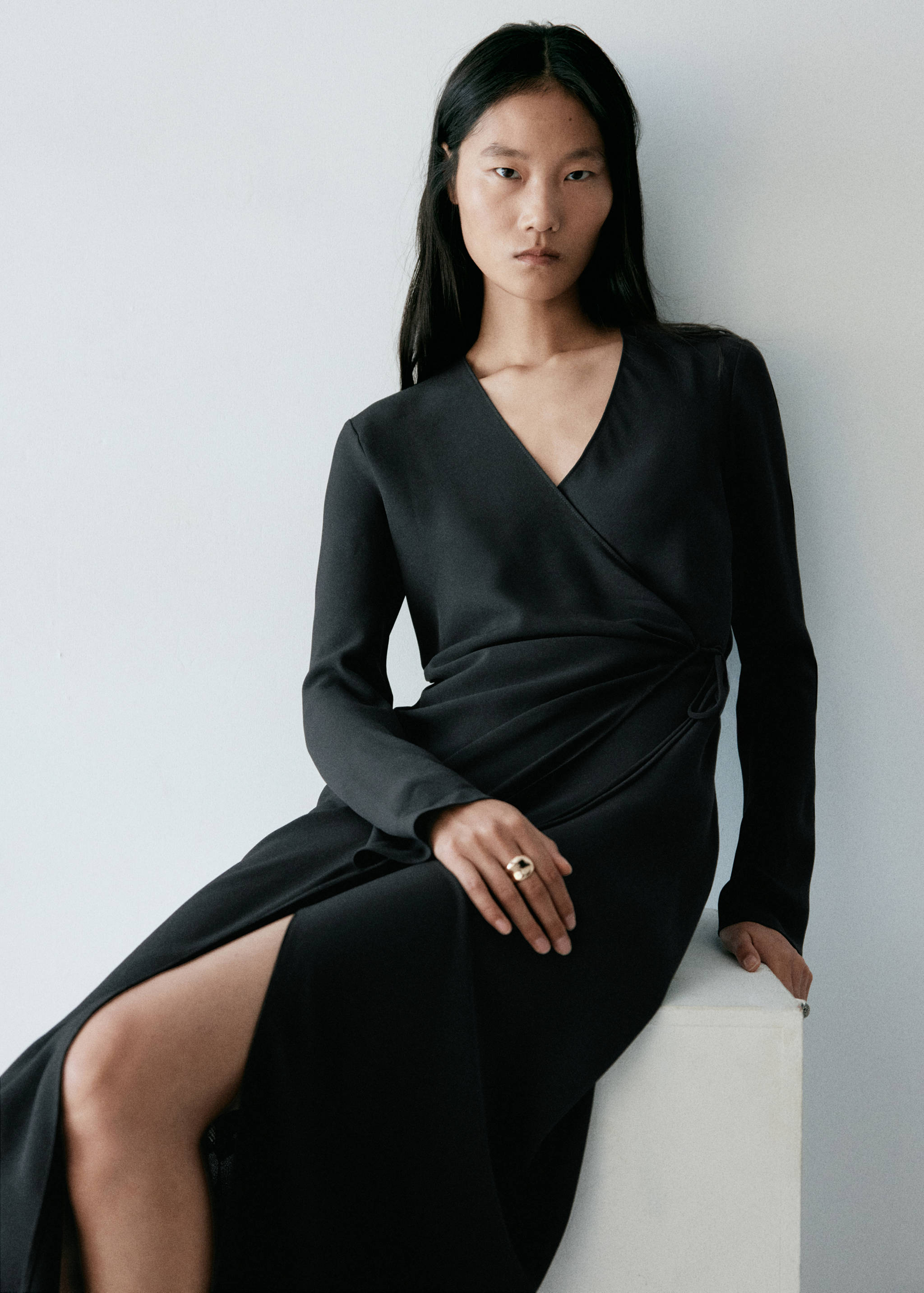 Vestido largo cruzado negro de manga larga con cuello en V, lazada lateral y abertura delantera.