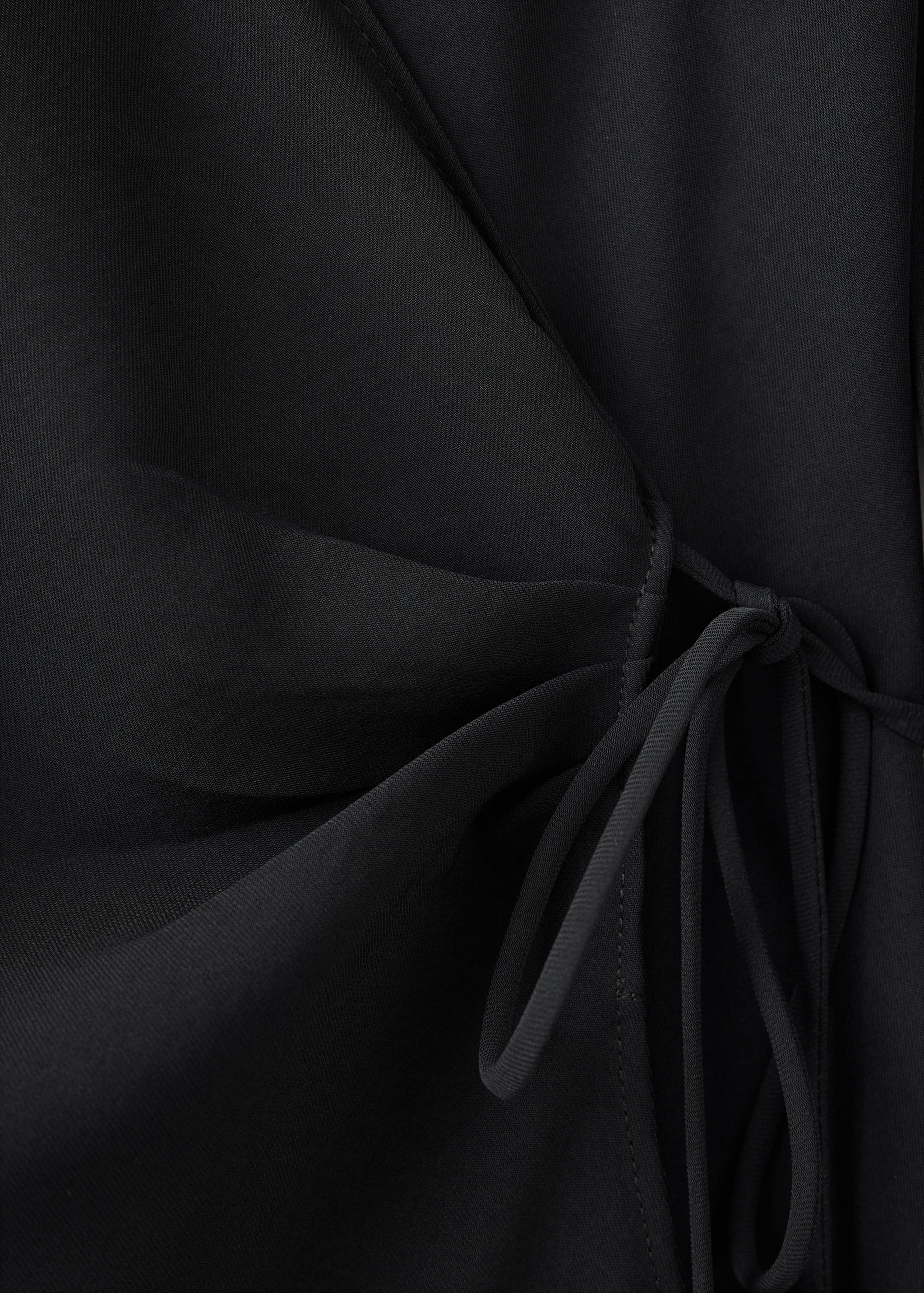 Primer plano de un vestido cruzado negro que muestra el cierre de lazada lateral.