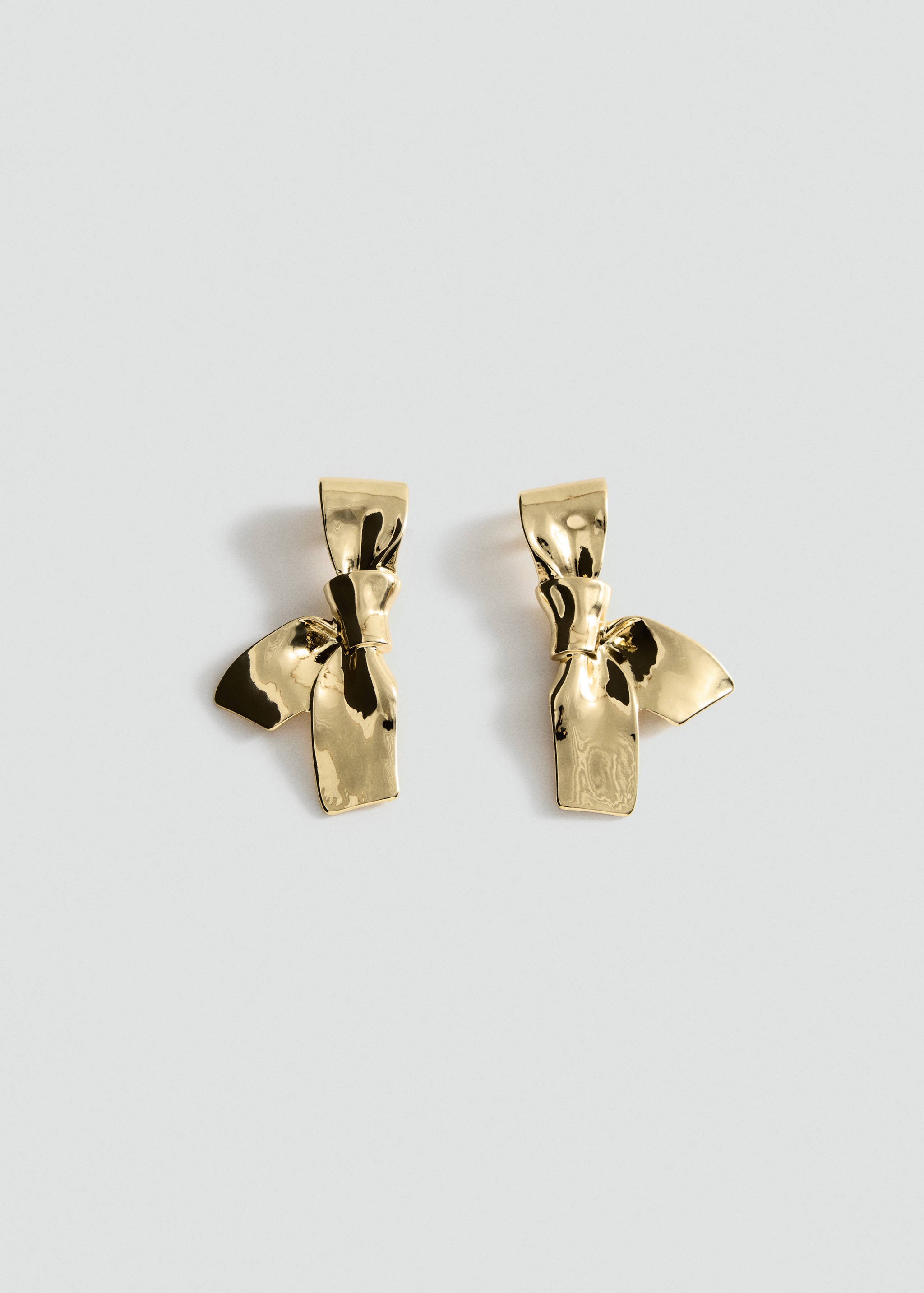 Glossy gold bow earrings in a still life view.