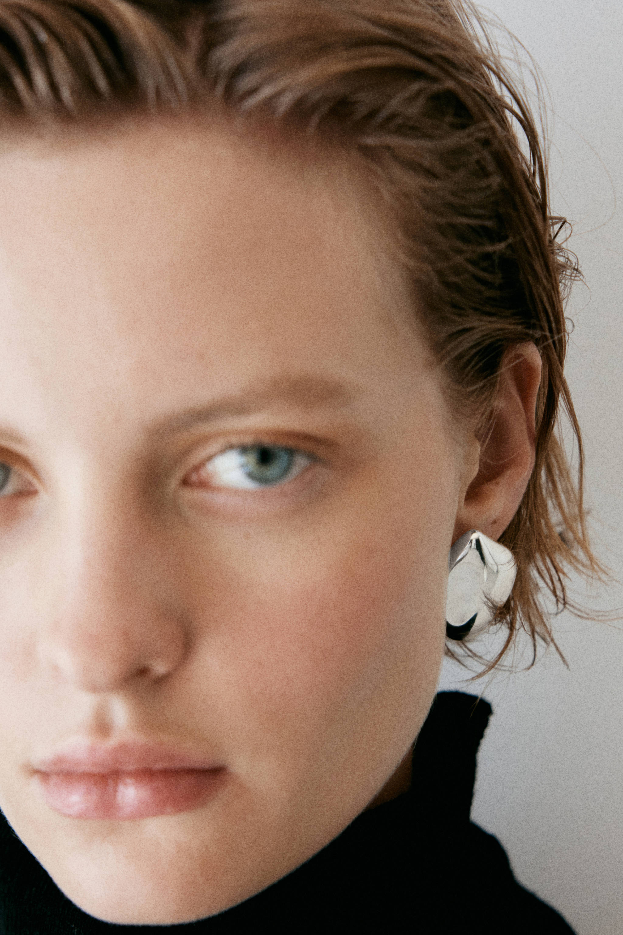Chunky silver-coloured metallic earring with an irregular geometric shape, worn on the ear.
