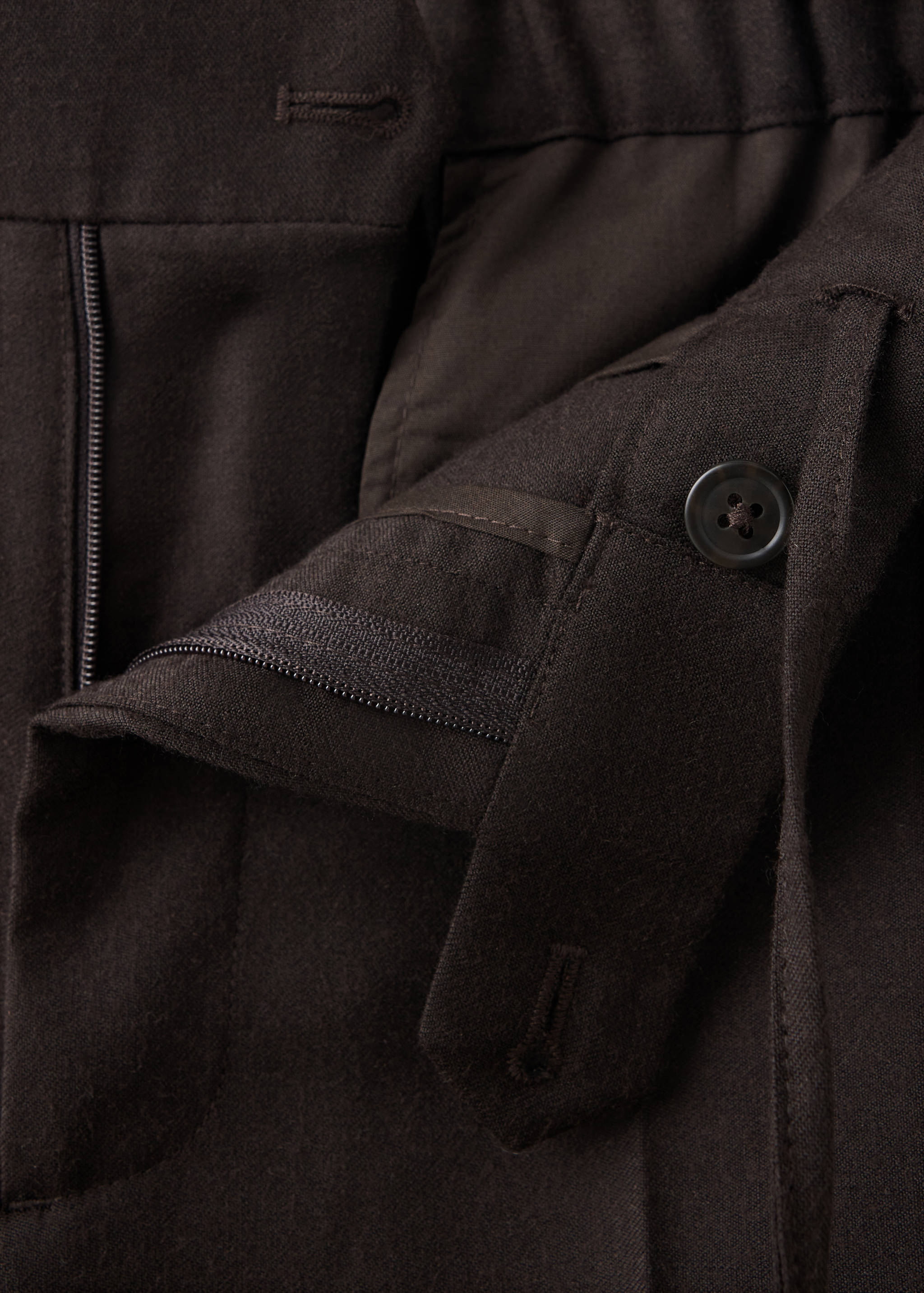 Close-up of the waistband and button fastening detail on dark brown trousers.