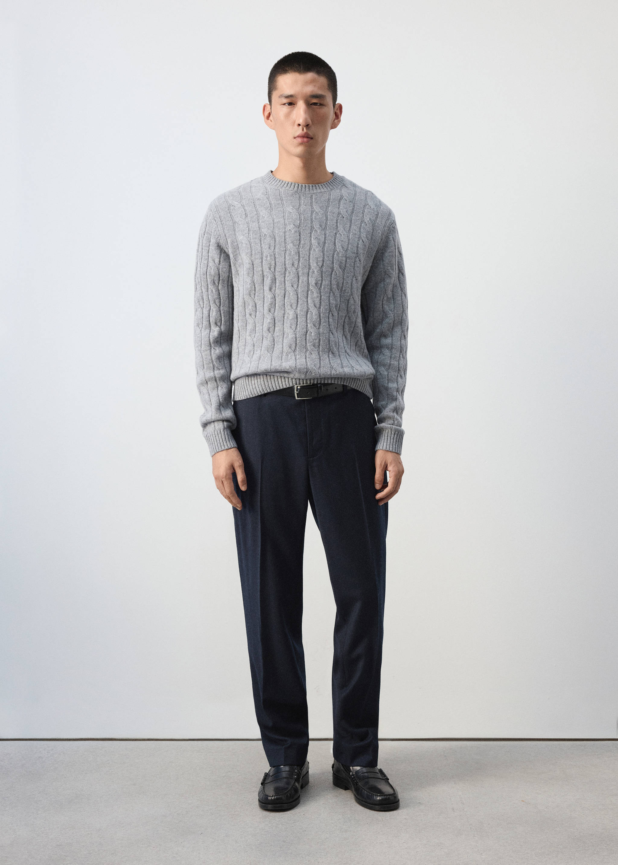 Dark navy blue trousers with straight-leg fit and pressed creases, worn with a grey cable-knit sweater.
