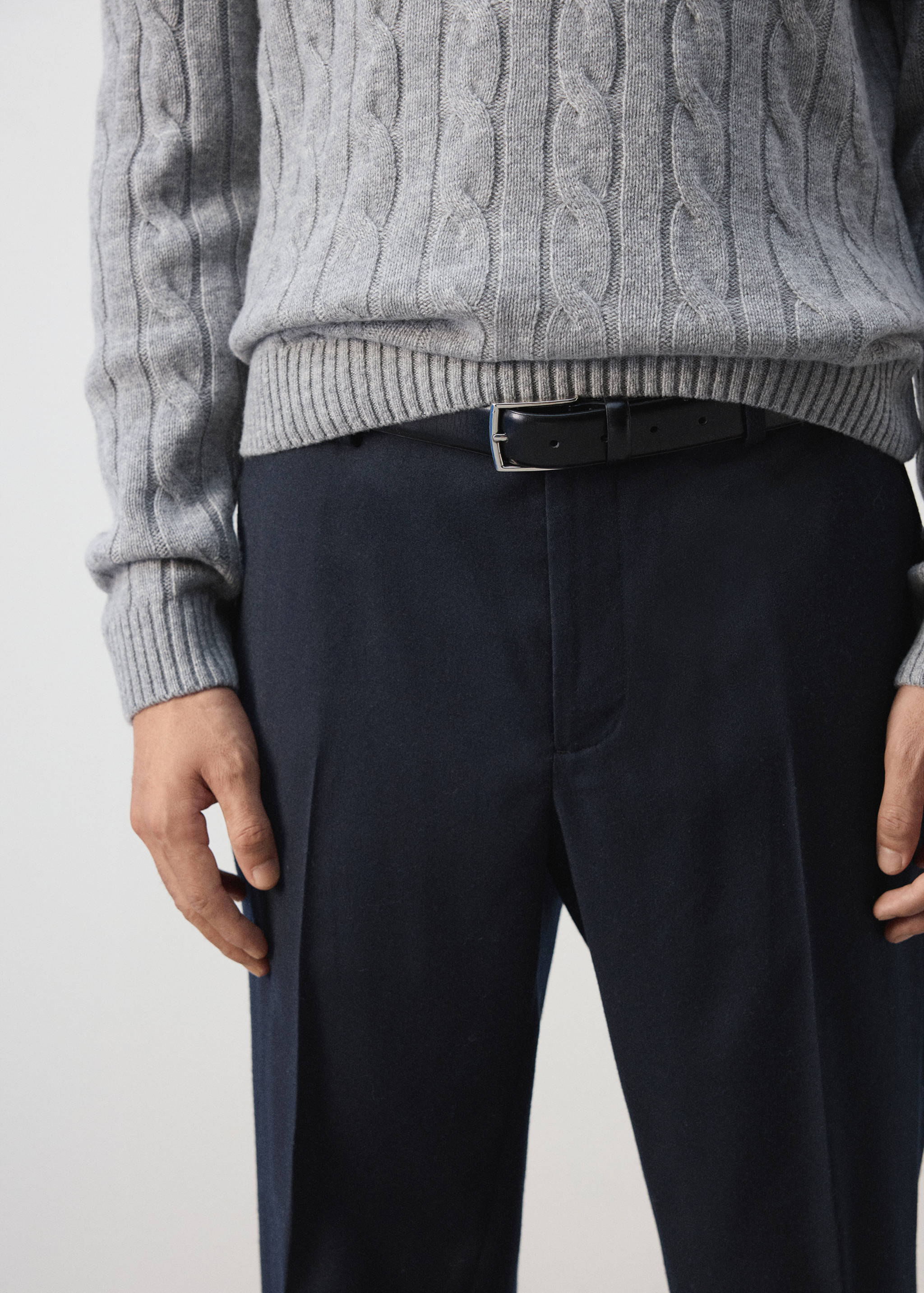Dark trousers with creases, styled with a black leather belt and grey cable-knit sweater.