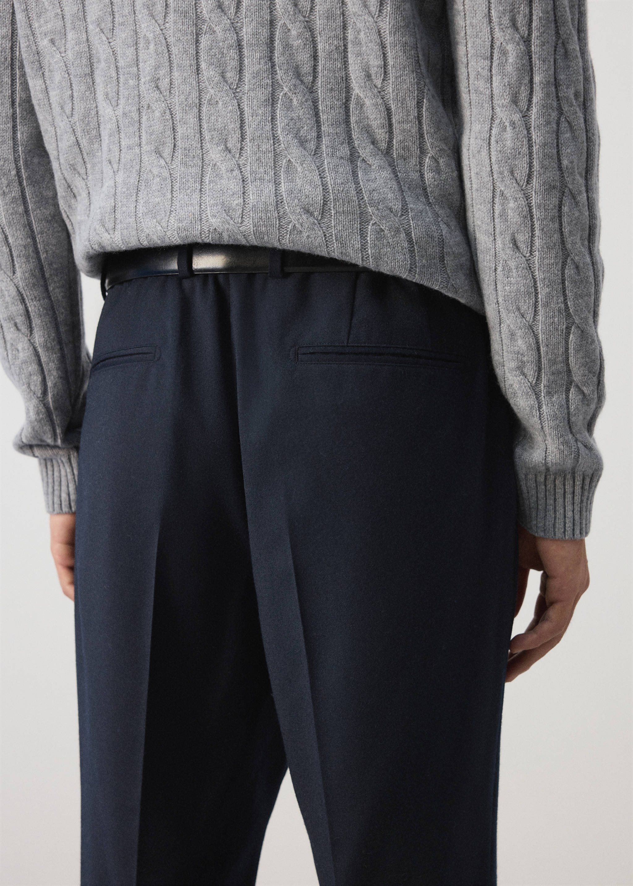 Dark navy blue trousers shown from the back, paired with a black belt and grey cable-knit jumper.