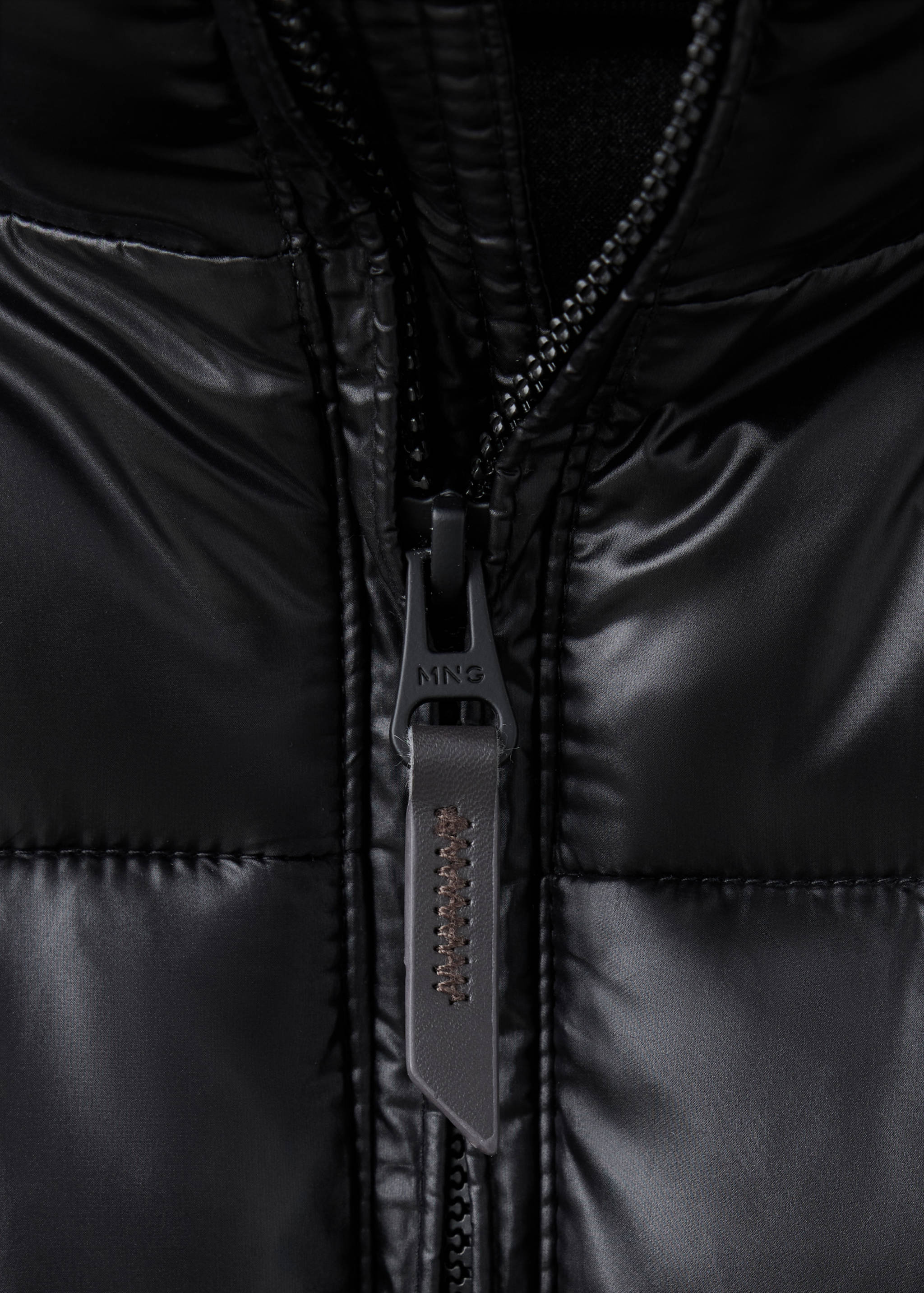 Close-up of a black anorak zipper detail with a branded MNG pull tab.