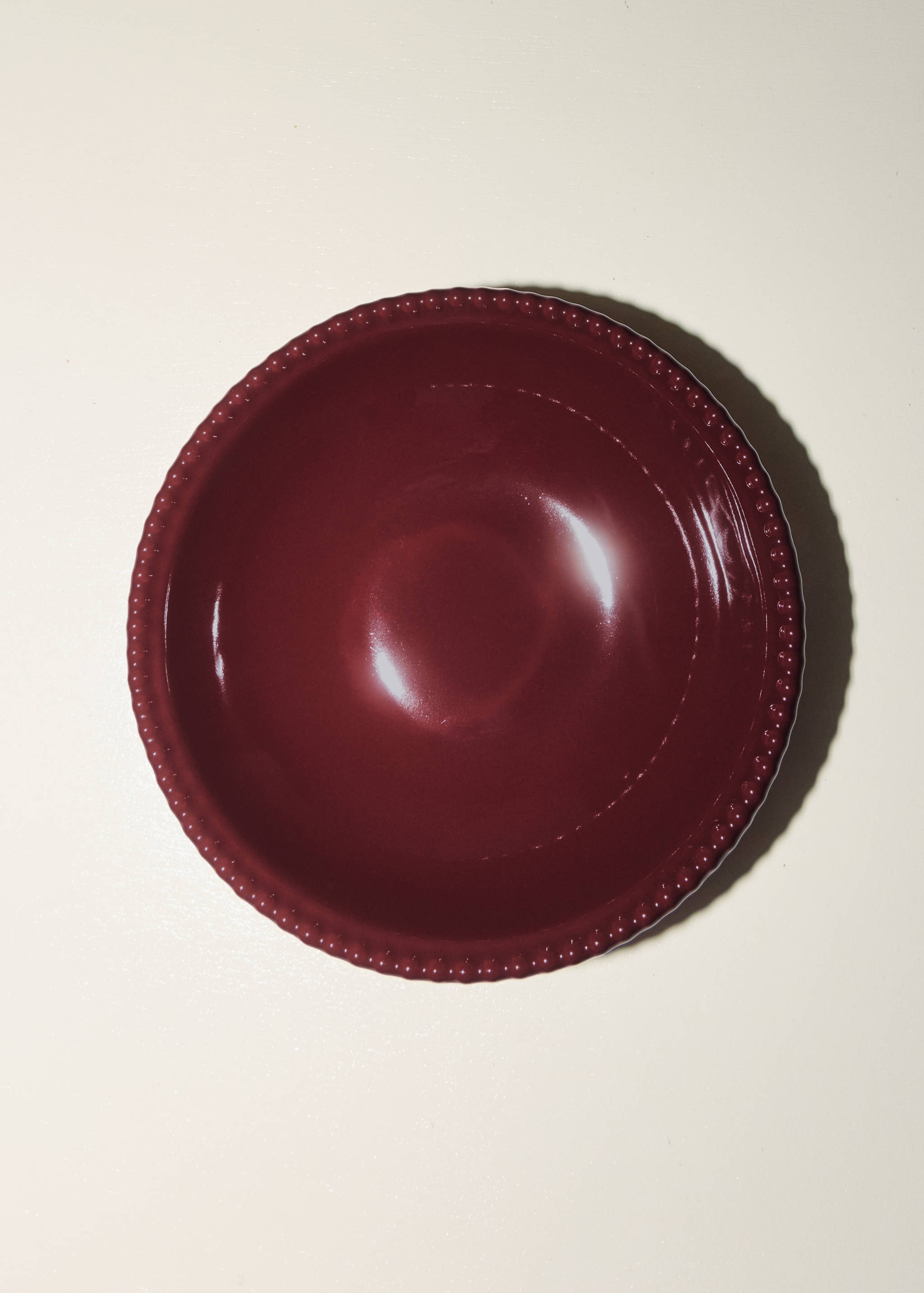 Burgundy round plate with a glossy finish and beaded trim.