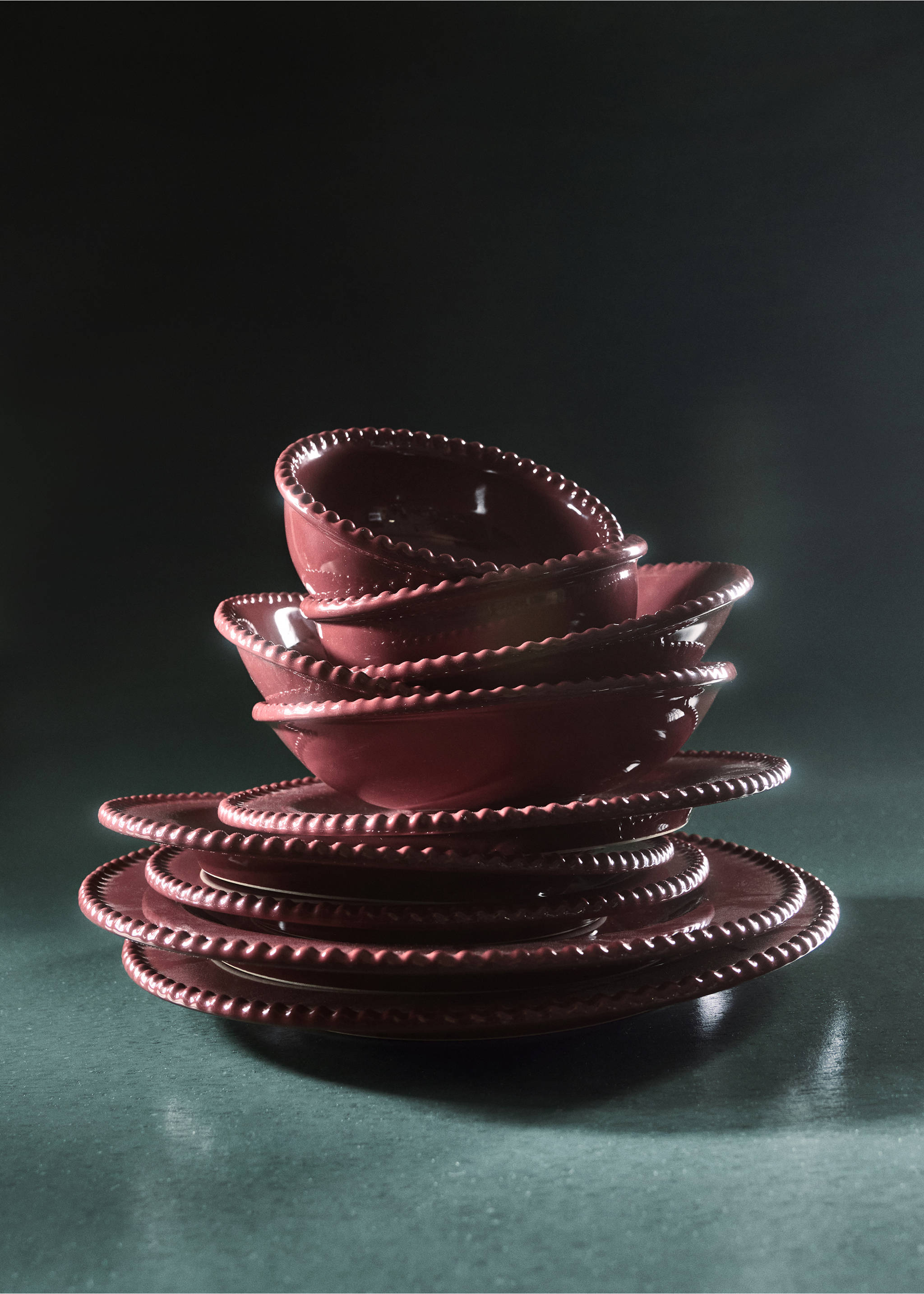 Stack of dark reddish-pink ceramic plates with beaded rims on a dark surface.