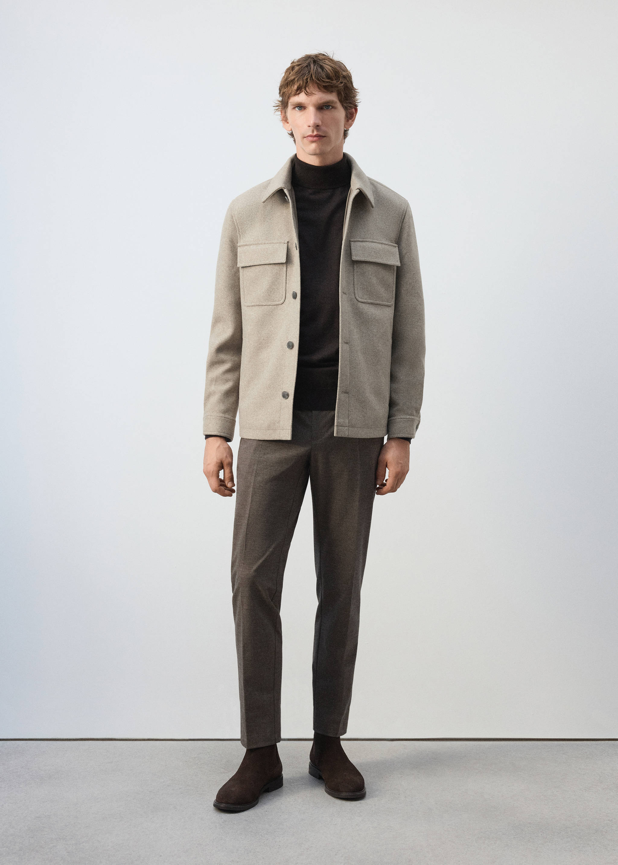 Brown trousers worn with a beige overshirt and dark roll-neck