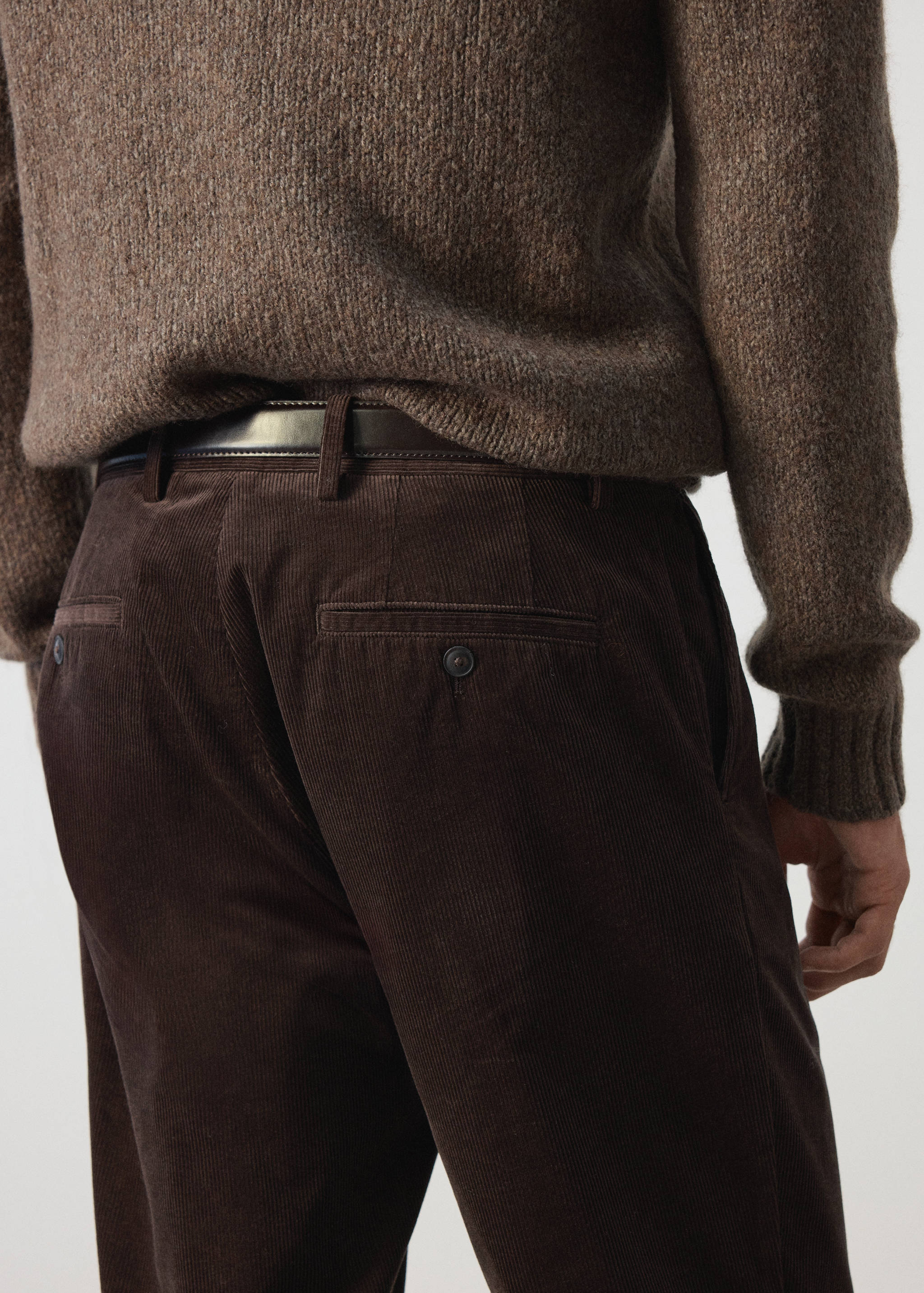 Pantalones de pana en marrón oscuro con bolsillos traseros de botón, vistos desde atrás con un jersey.