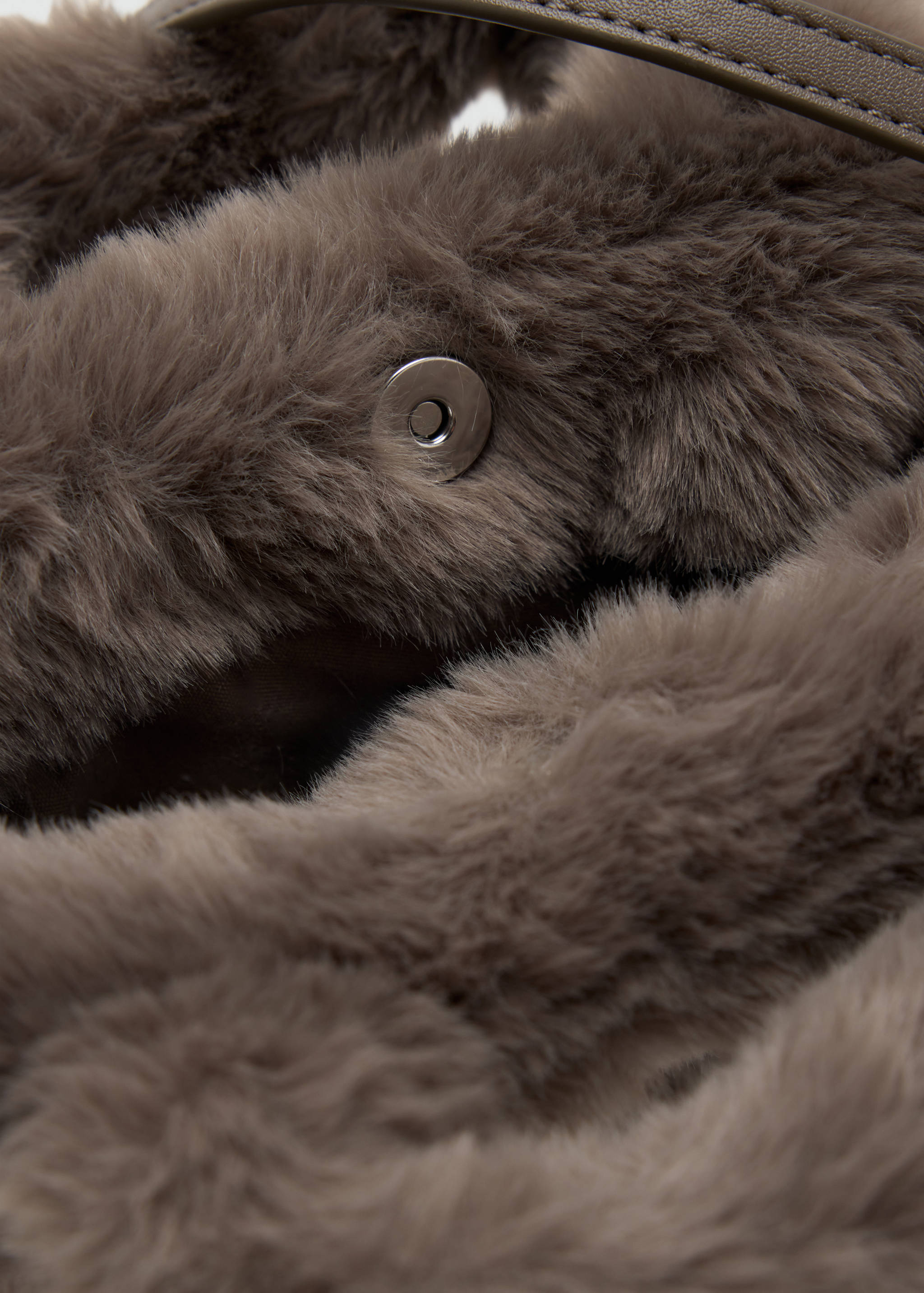 Close-up of a taupe faux-fur mini bag showing its snap closure detail.