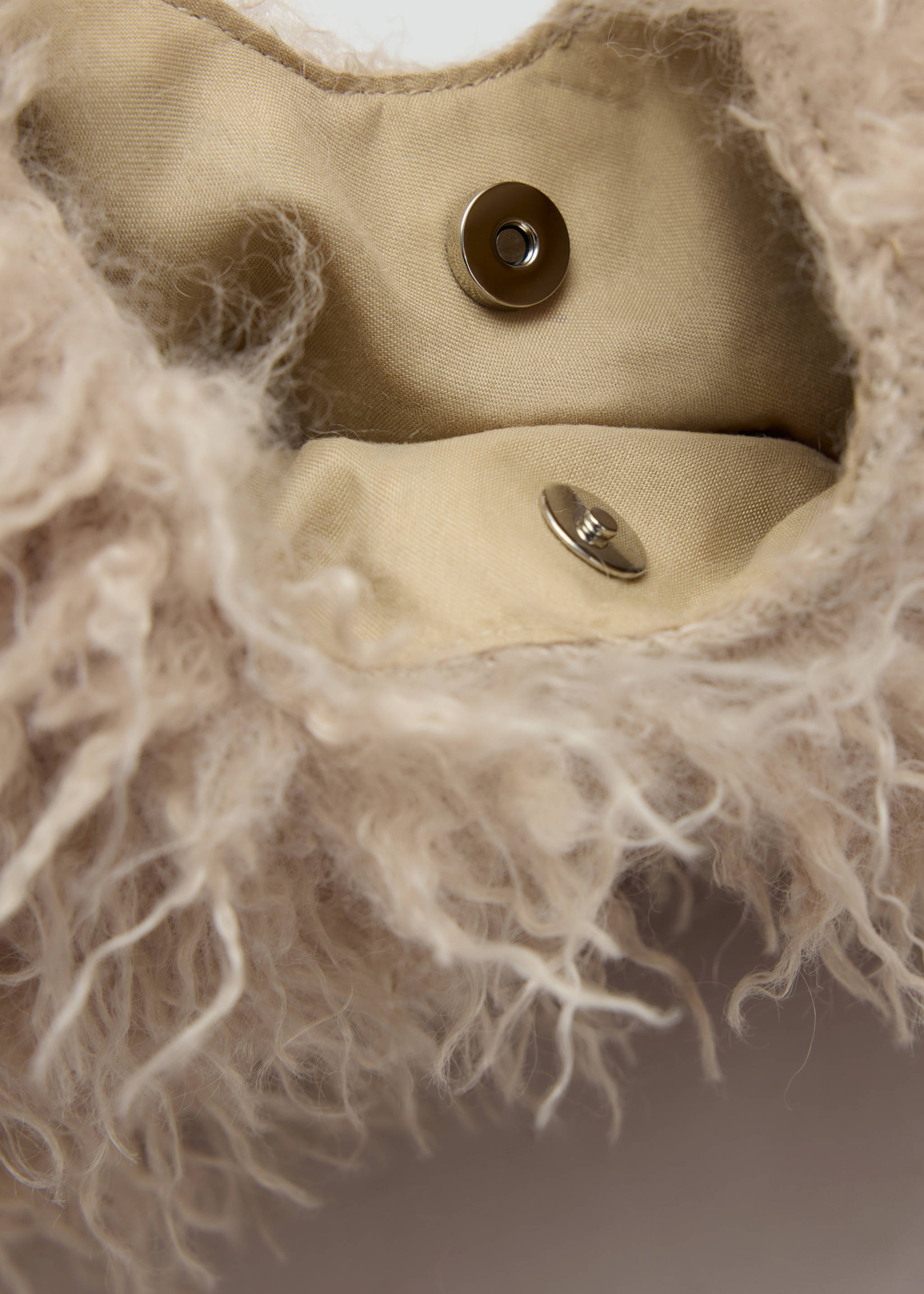 Close-up of the magnetic clasp and lining inside a beige faux-fur mini bag.